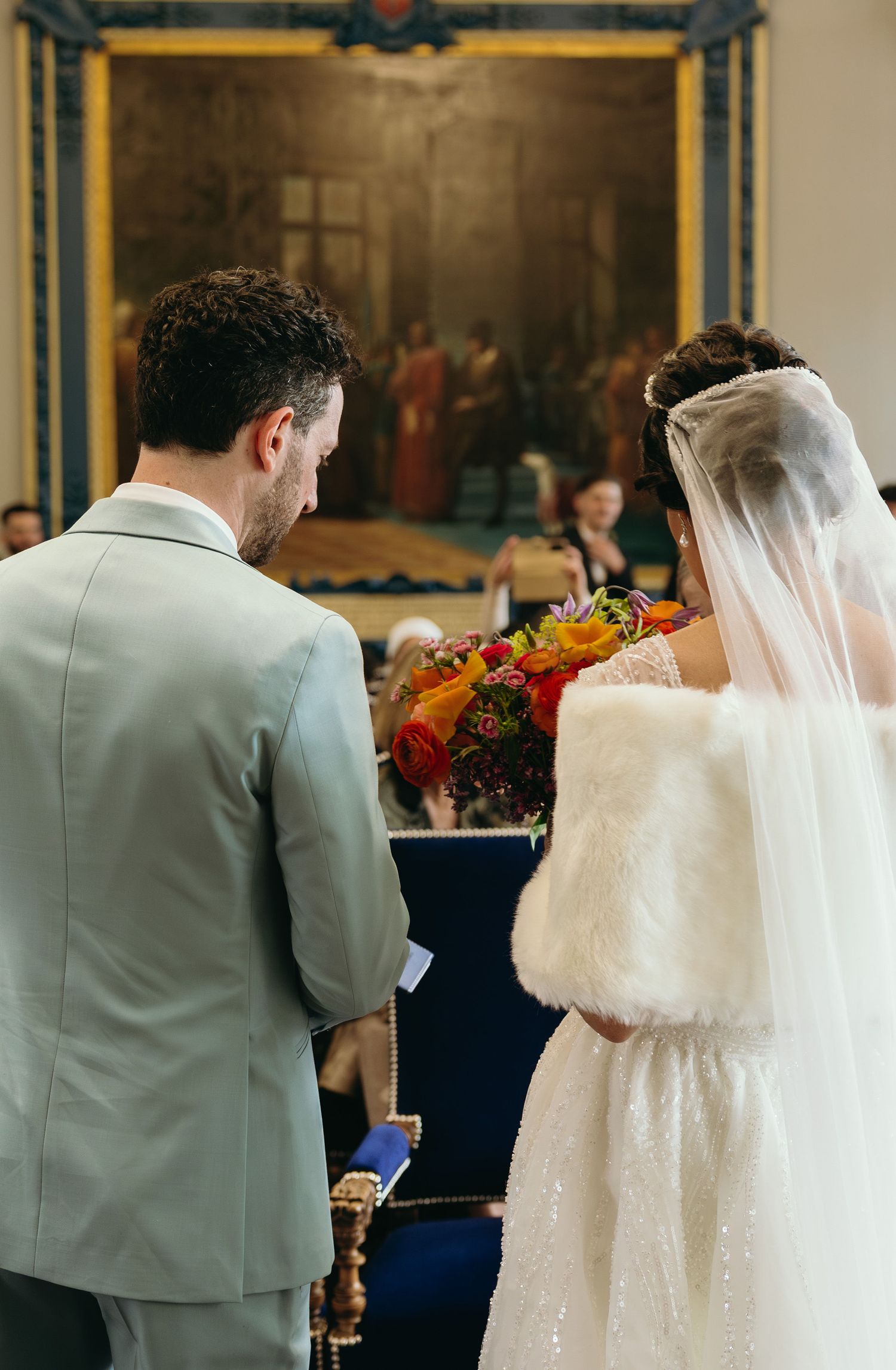 Cérémonie de mariage élégante dans un hall orné avec œuvres encadrées en or et costumes gris clair à Angers