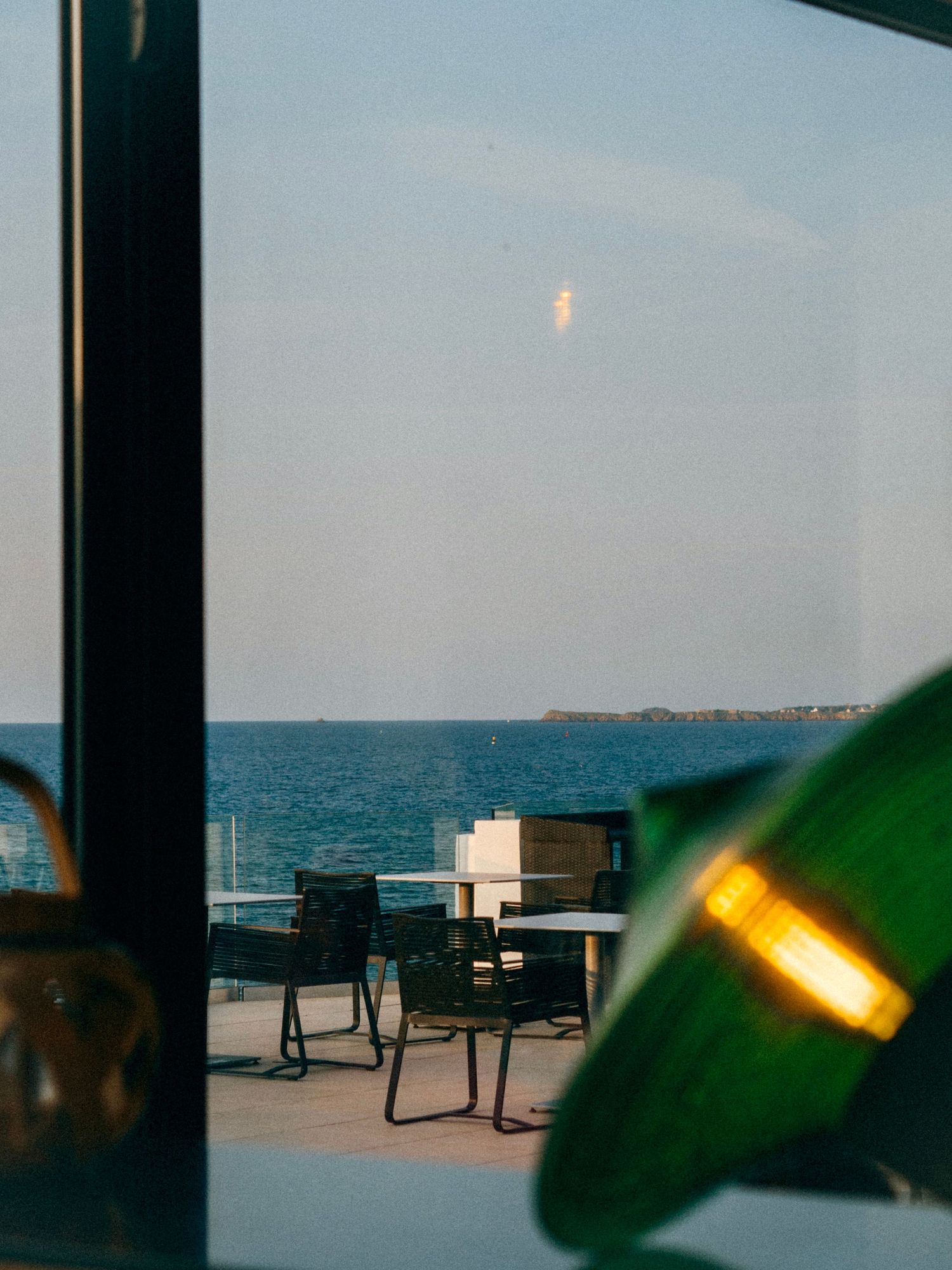 Hotel dinard Vue sur l’océan à travers une fenêtre avec la lumière du coucher de soleil.