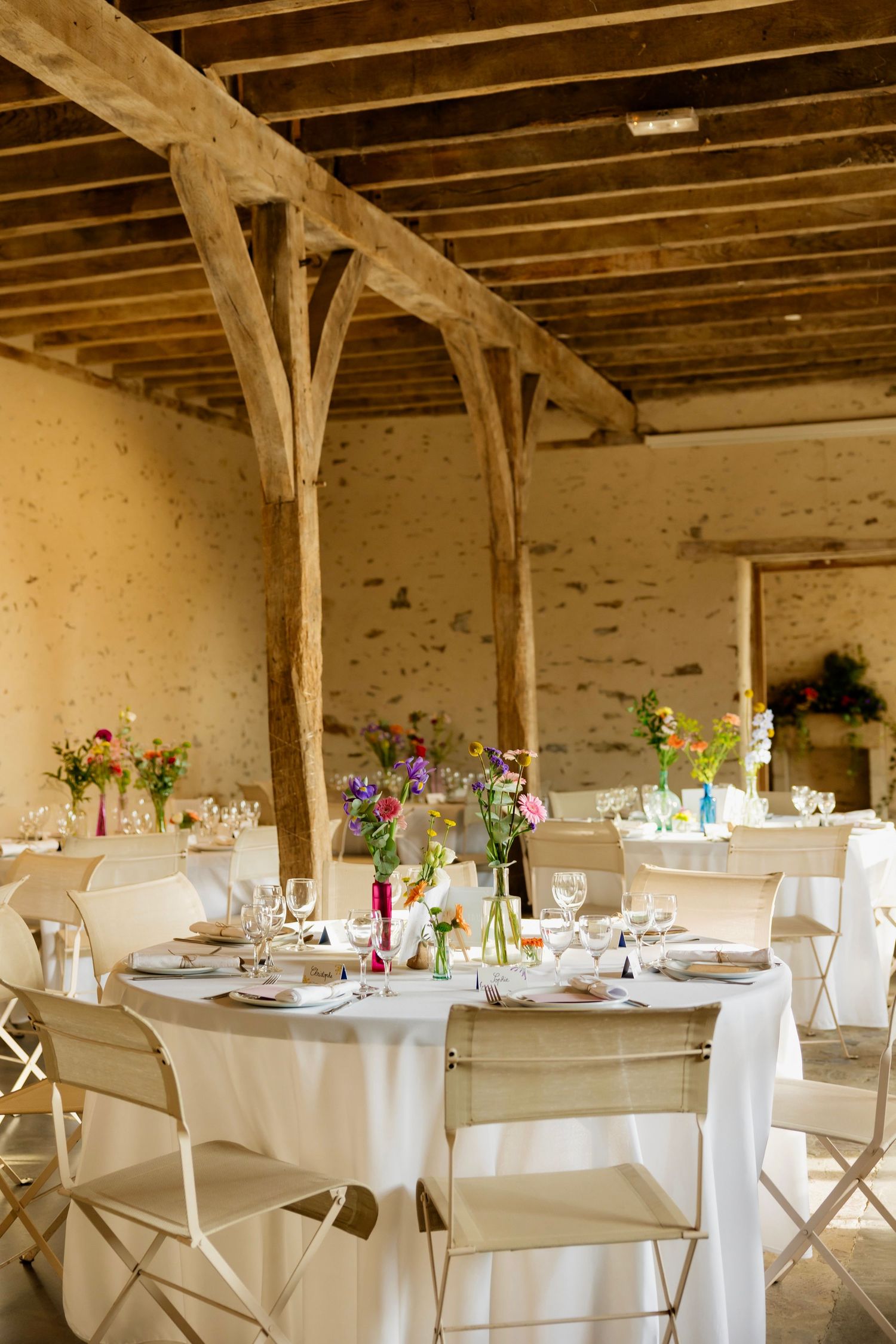Elegant rustic wedding reception venue with round tables, white linens, and colorful floral centerpieces.