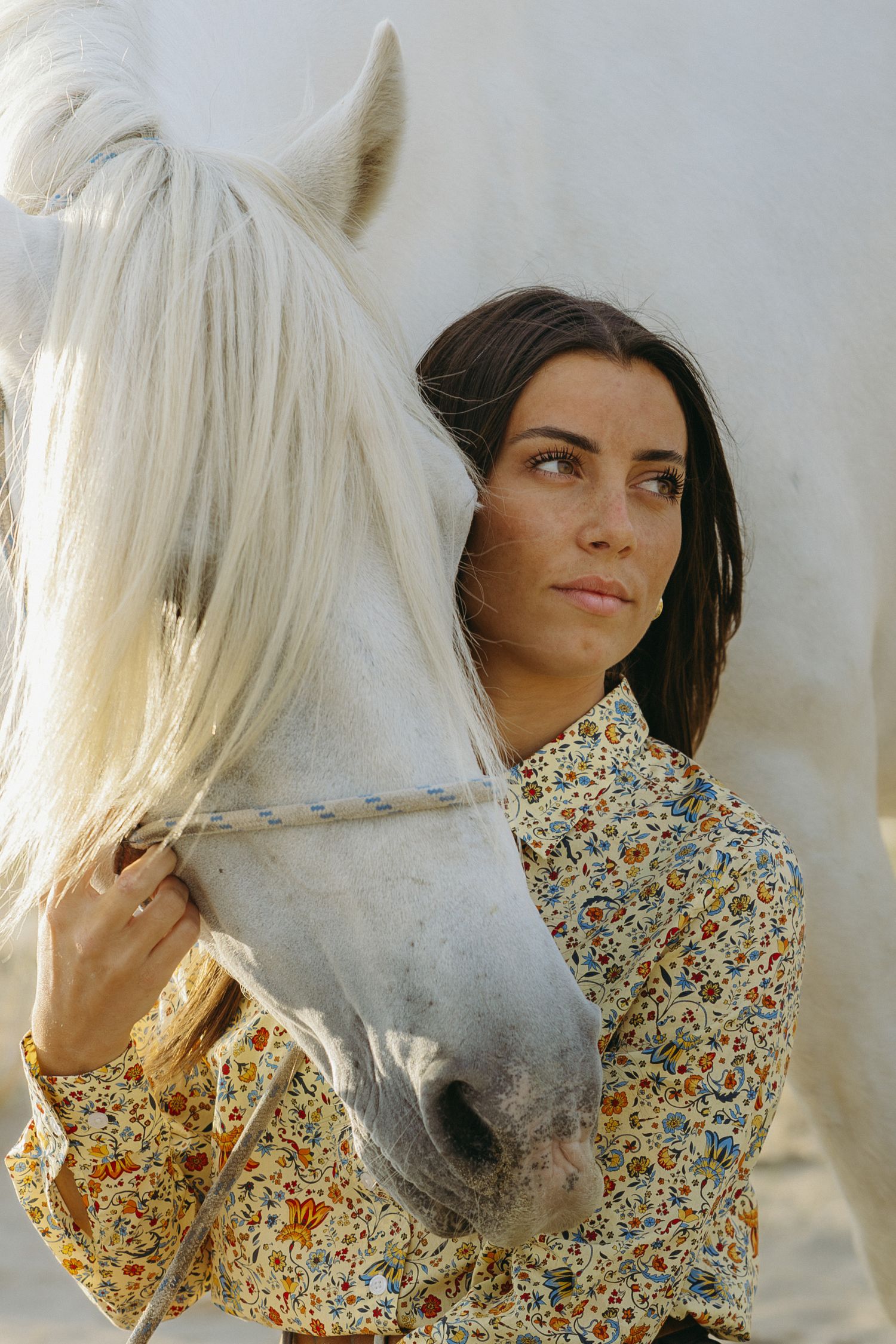 A white horse and person in a floral dress share a tender moment against a light background.