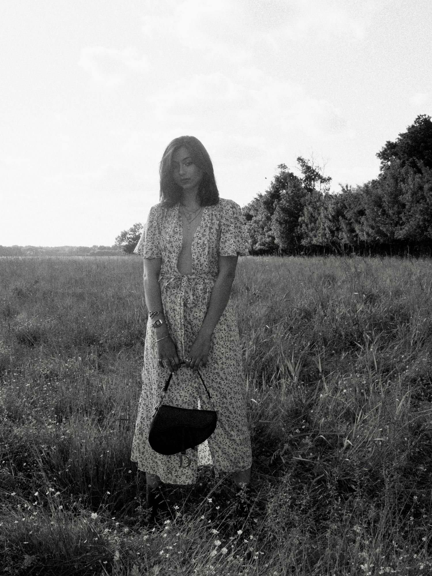 Black and white photograph of someone walking through a wildflower field wearing a floral dress.