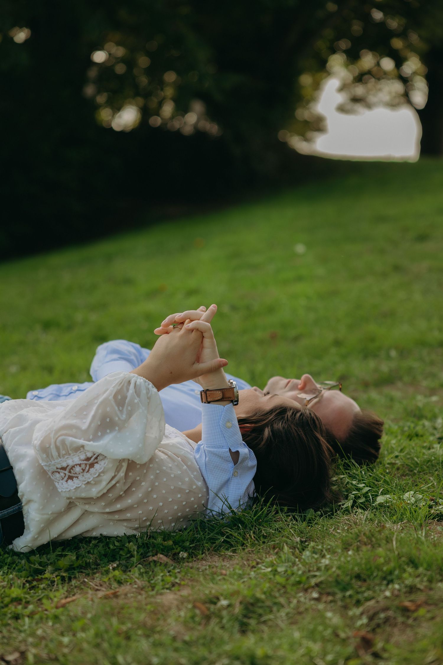 A couple lying on grass holding hands while looking up at the sky on a sunny day.