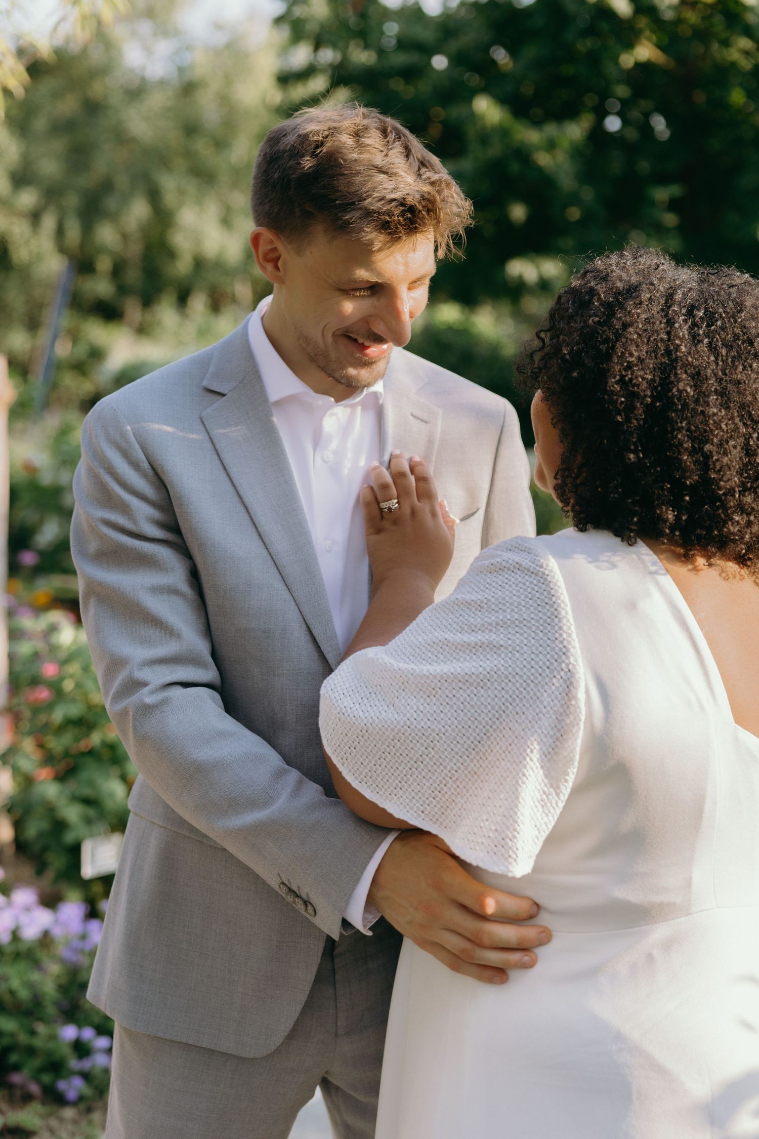 A couple in elegant wedding attire share an intimate embrace in a garden setting.