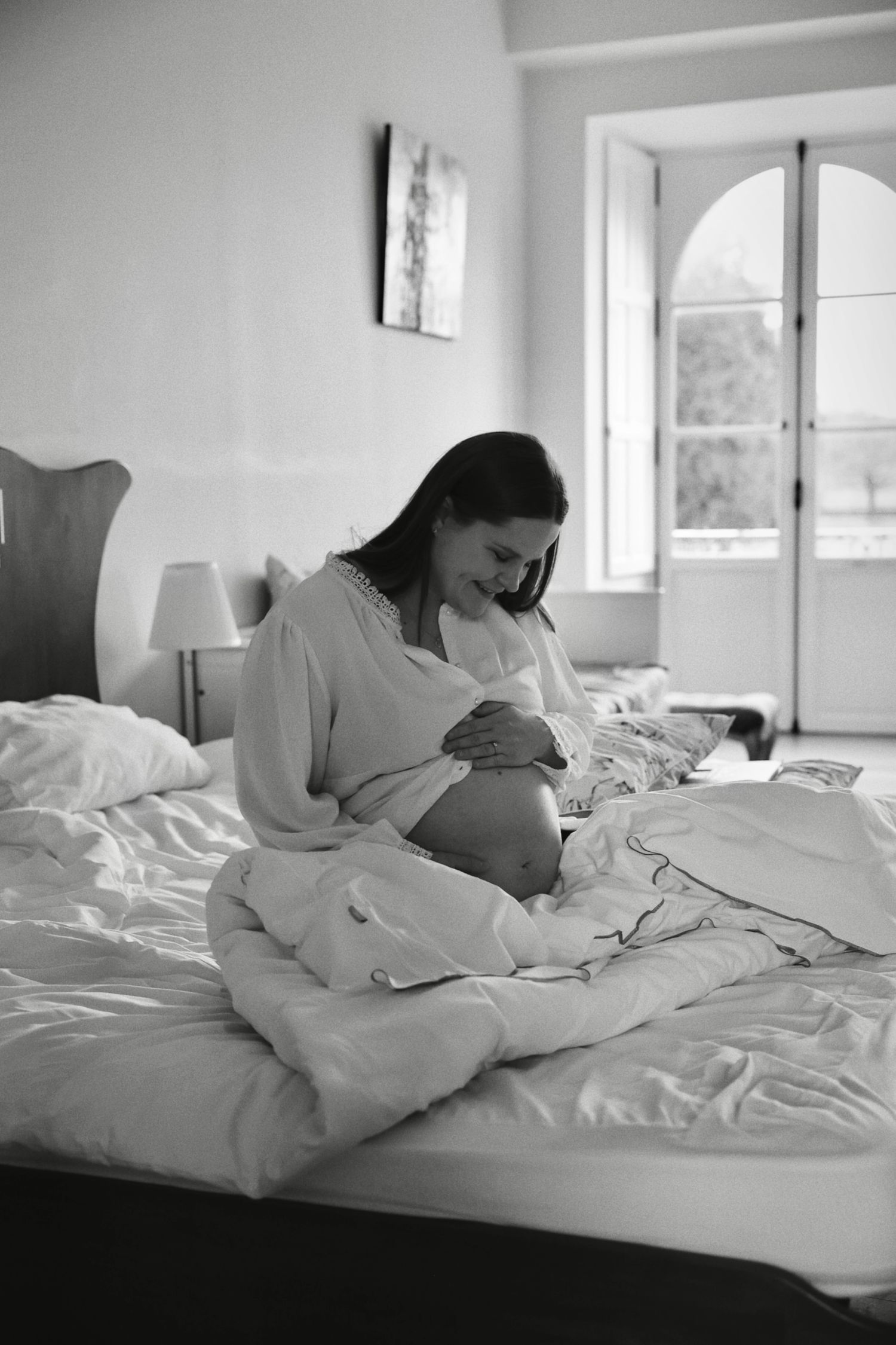 Black and white photo of an expectant mother sitting peacefully on a bed.