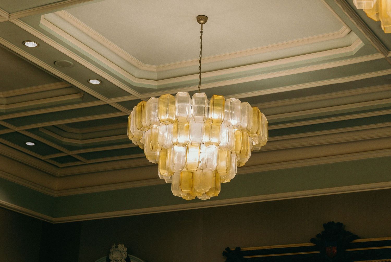 Ornate ballroom ceiling with crystal chandeliers and decorative molding in warm lighting.