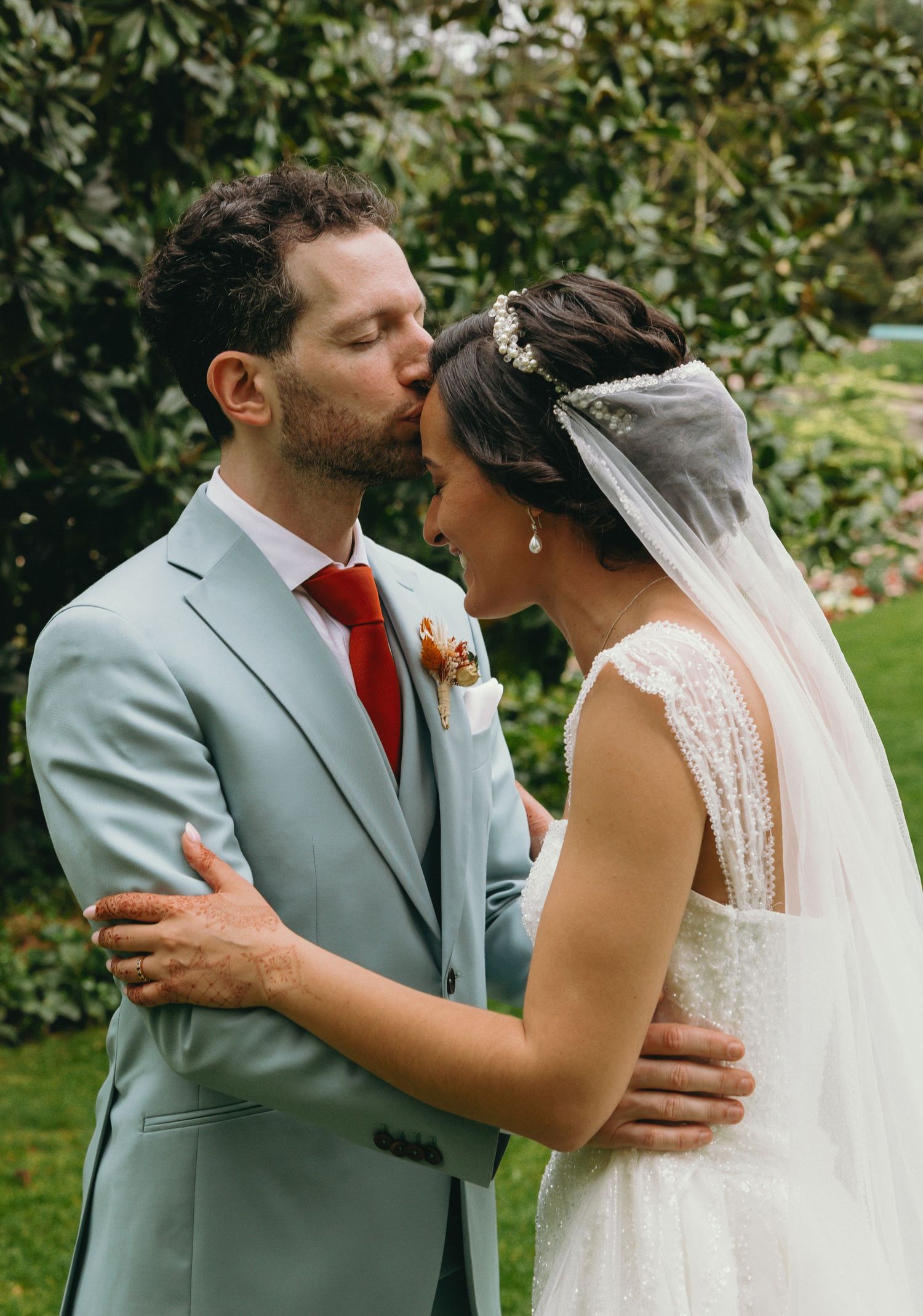 A tender wedding moment captured in a garden with the couple in gray suit and white dress.