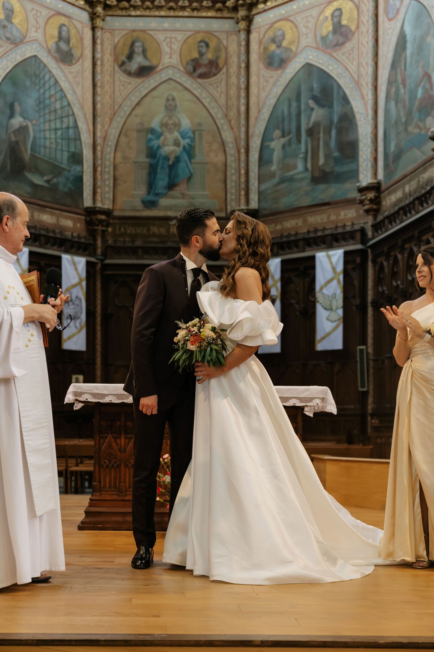Bride and groom share first kiss at ornate church altar, surrounded by stunning Byzantine murals and religious artwork.