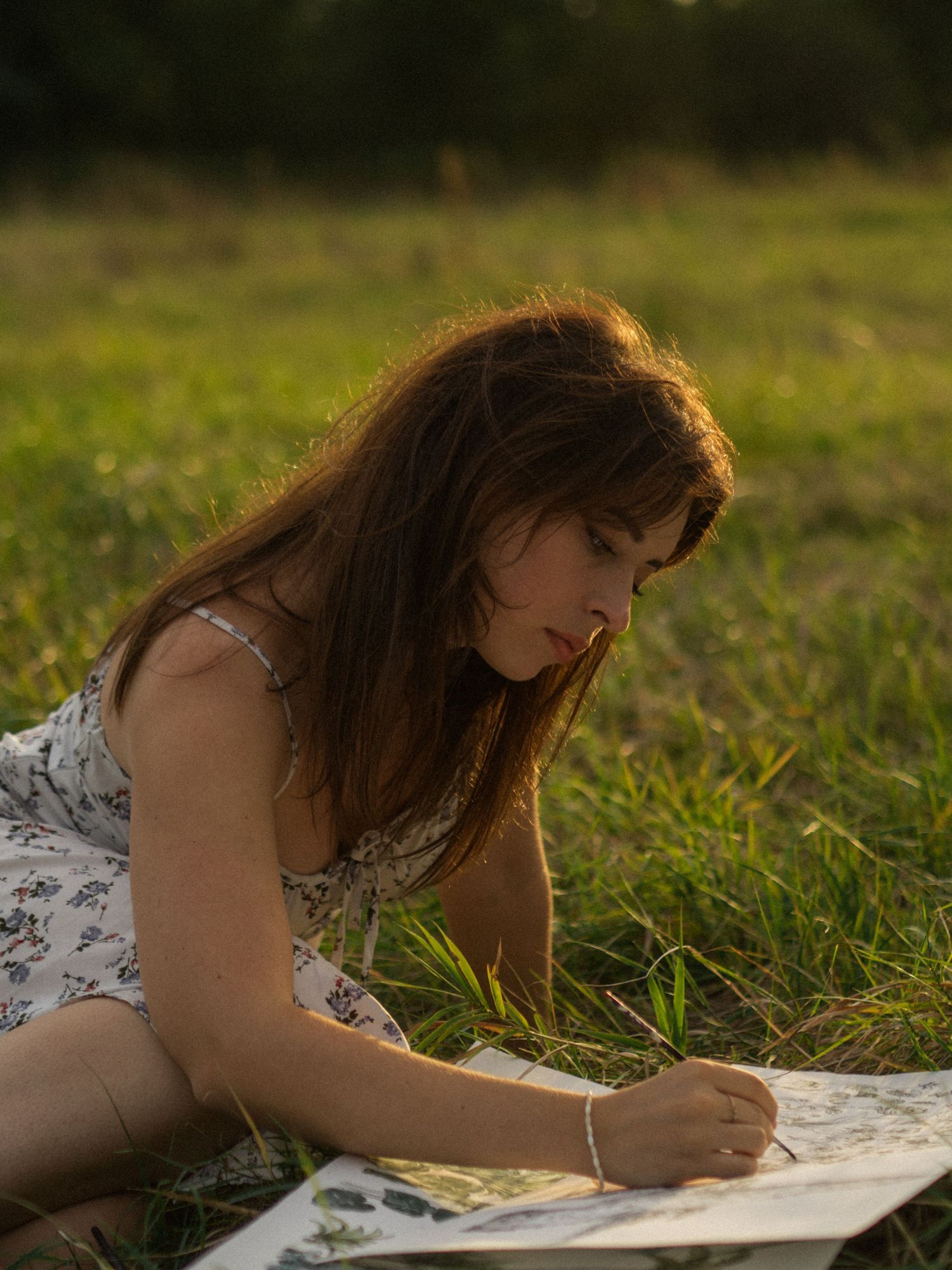 A person lies on grass while writing in a notebook during golden hour.