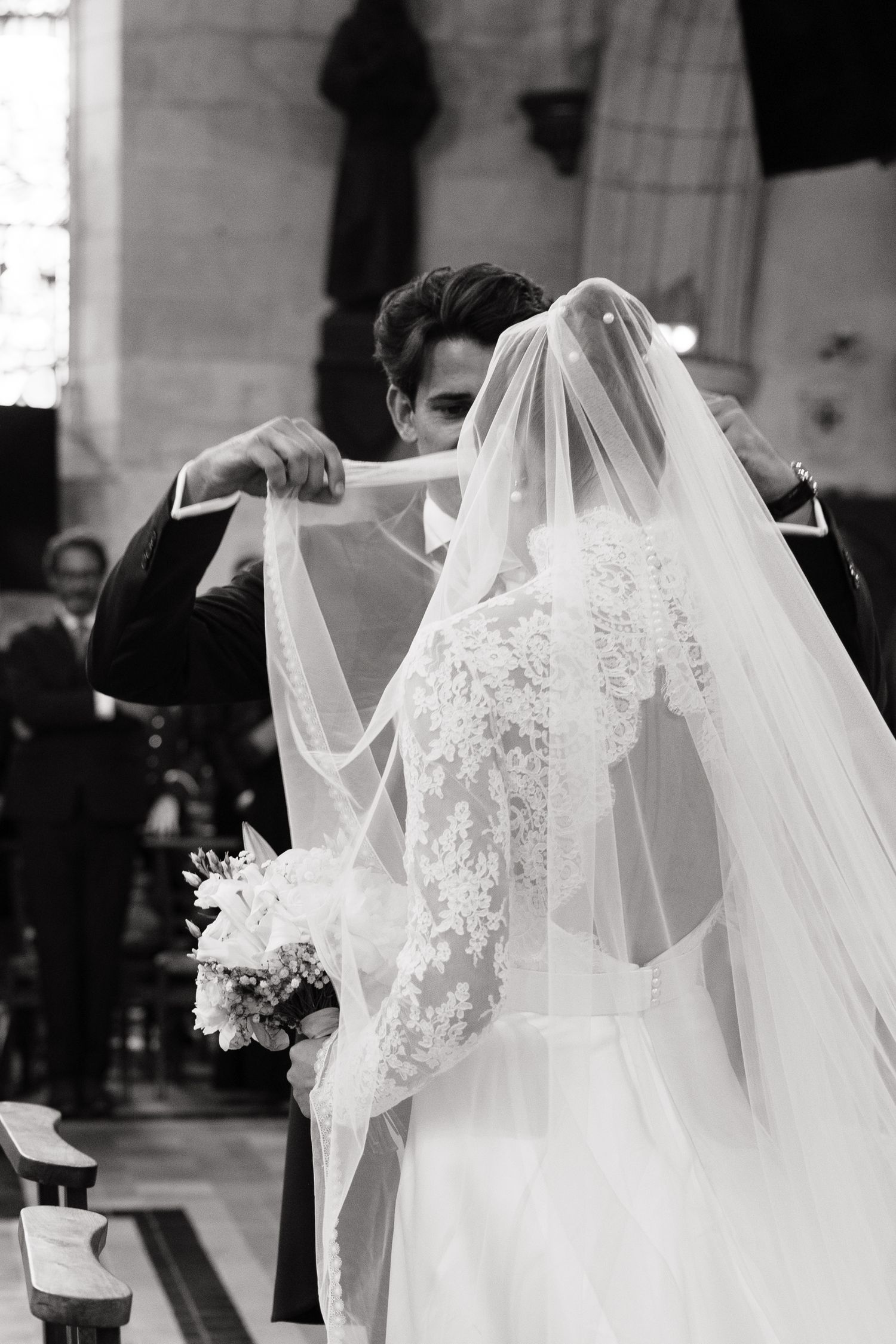 Groom lifting bride's lace veil during church wedding ceremony, black and white photo.