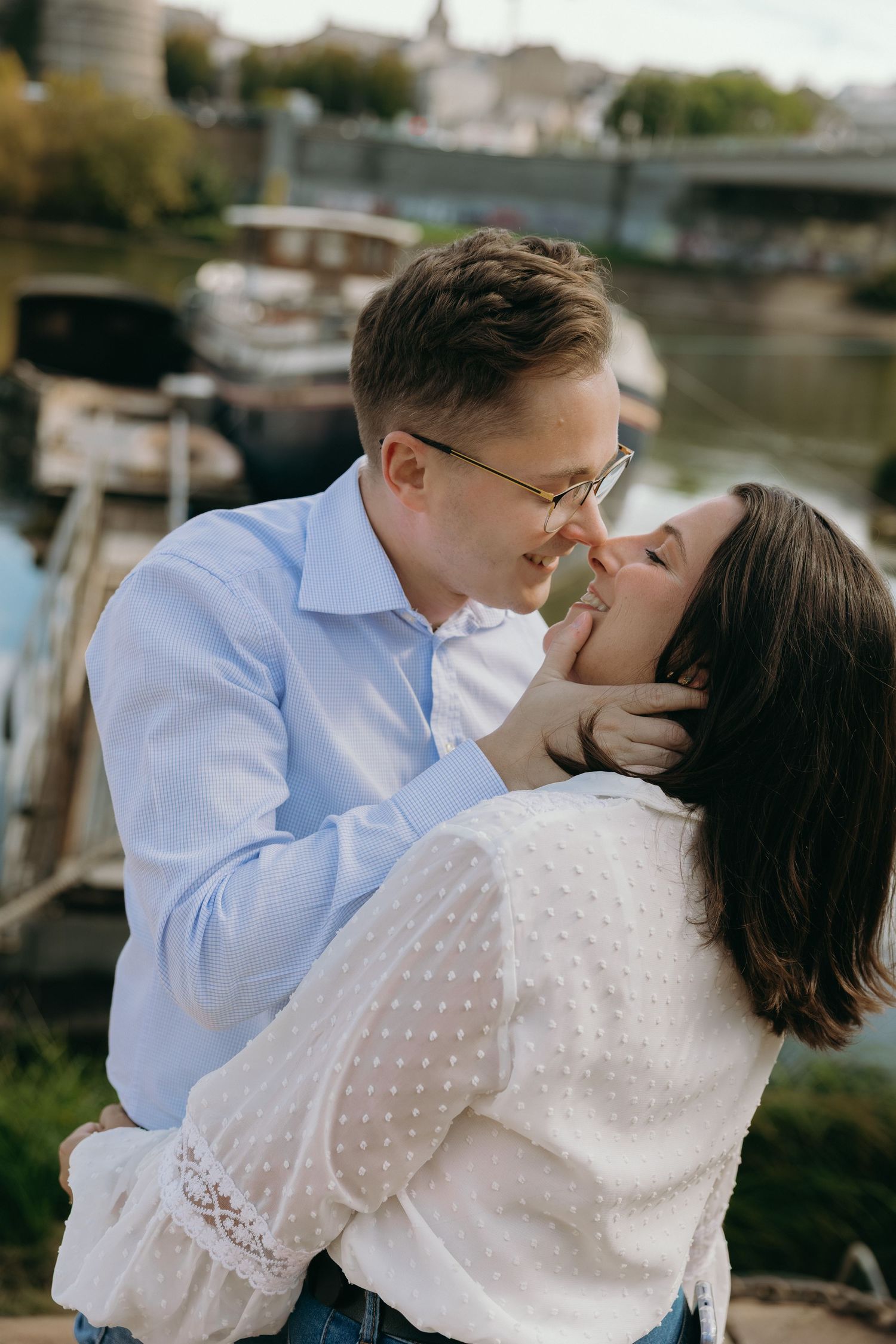 A romantic embrace captured by a waterfront with boats visible in the background.