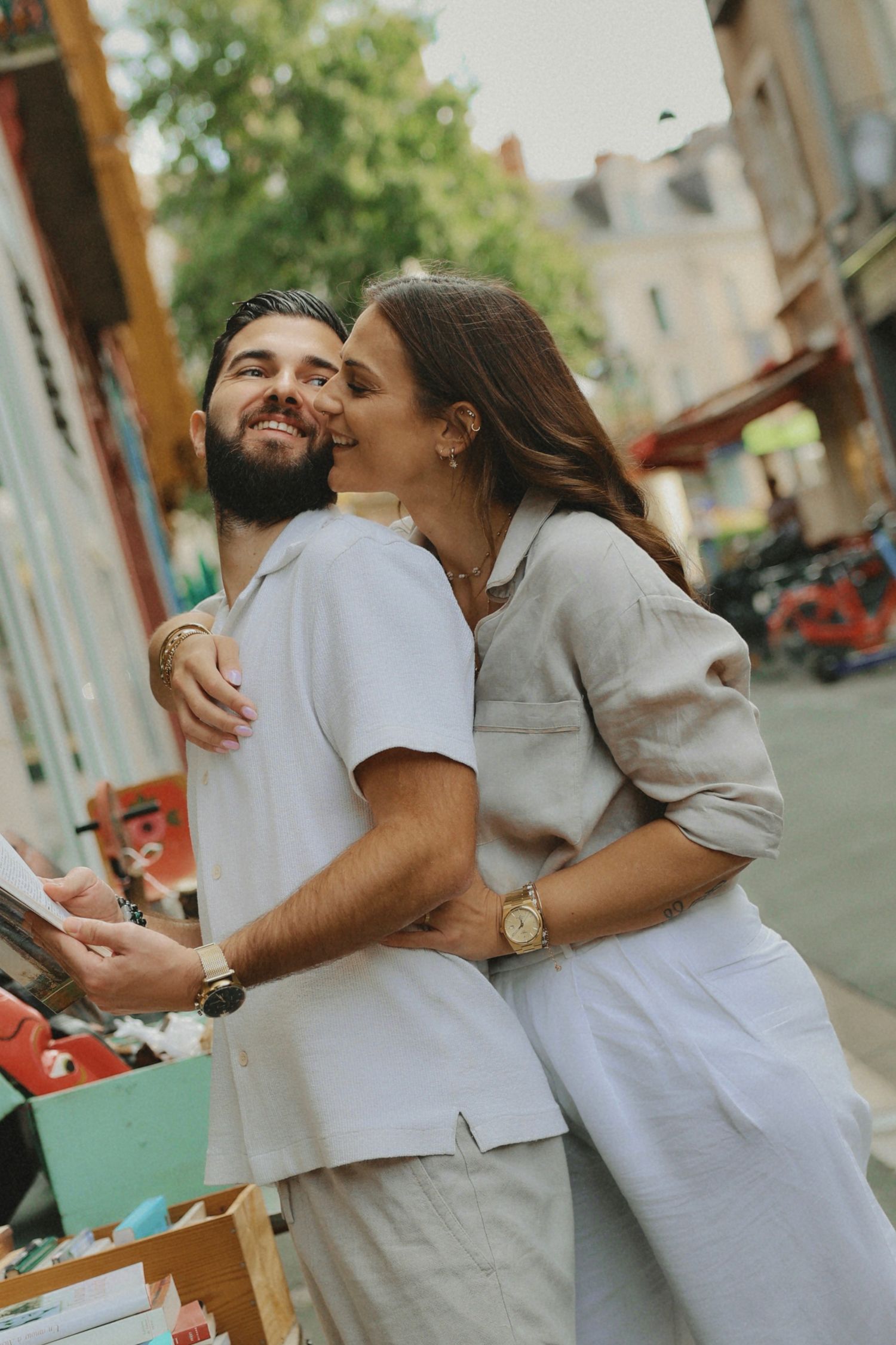 A couple wearing light colored outfits shares joyful moments on a city street.
