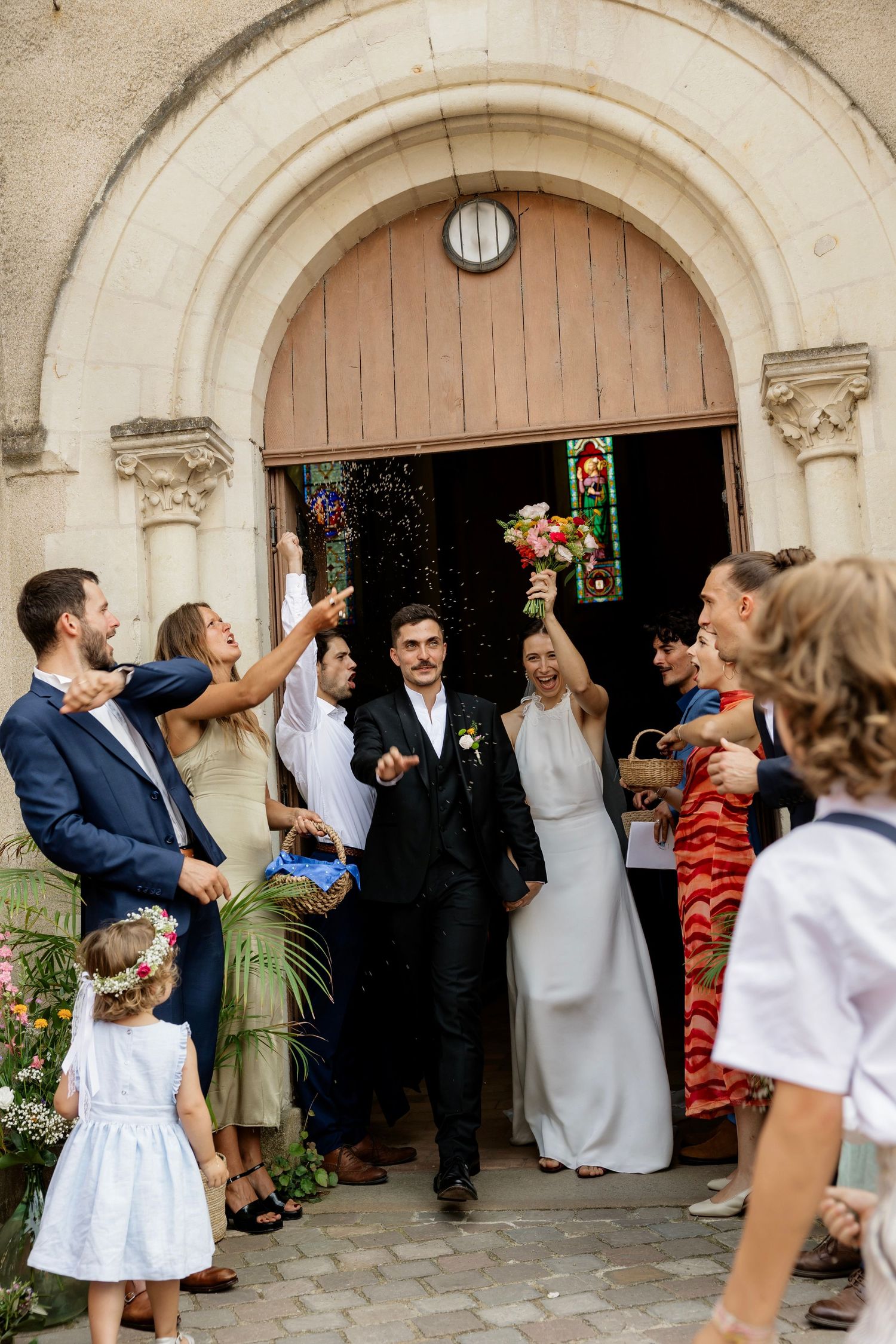 Newlyweds exit church greeted by cheering guests throwing confetti after wedding ceremony.