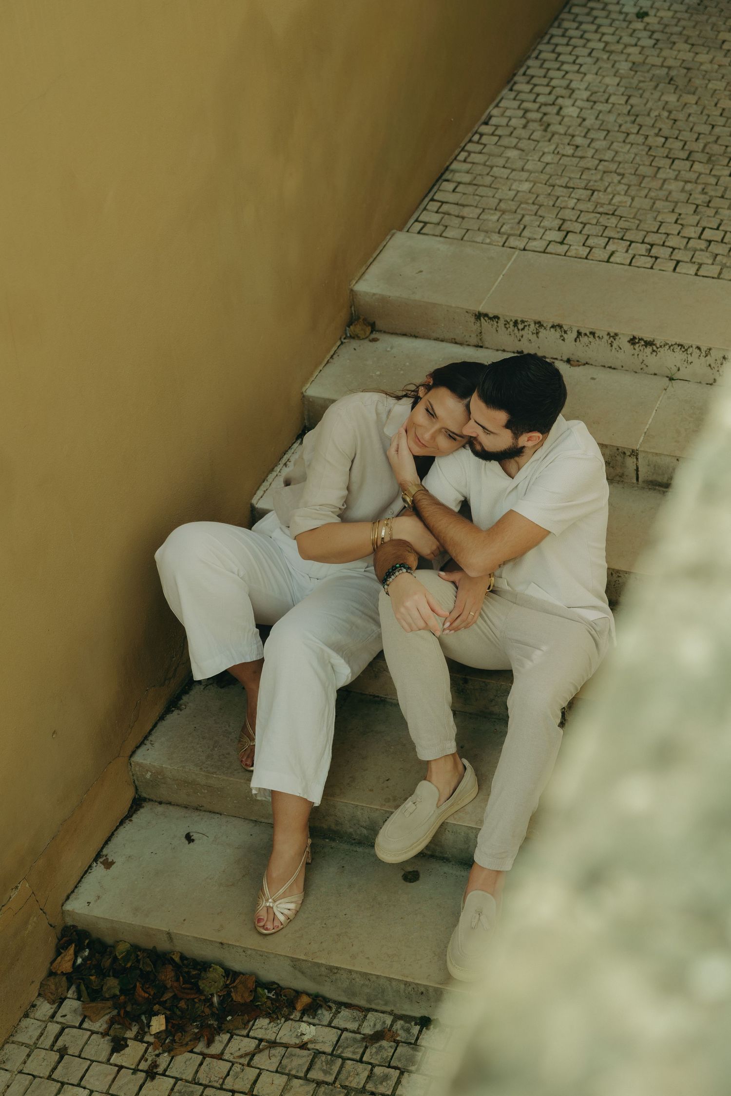 A romantic couple in white outfits sharing intimate moments while sitting on stone steps.