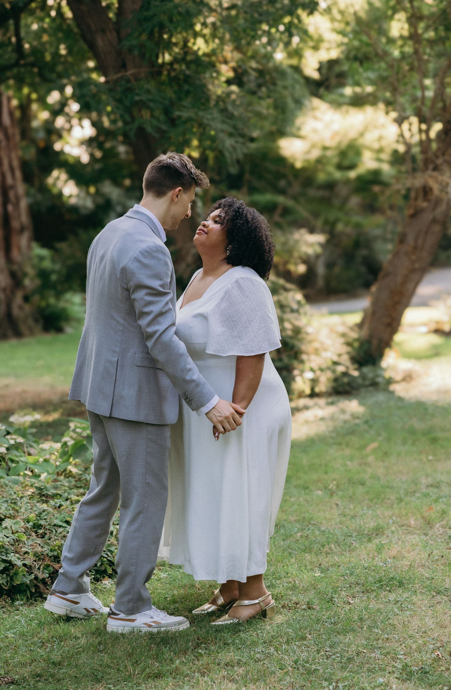 A couple in grey and white attire share a joyful moment in a sunlit garden.