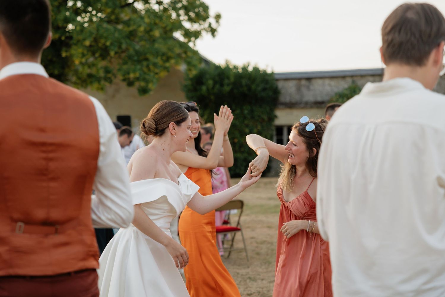 Bride dancing and laughing with guests in colorful dresses at an outdoor wedding reception.
