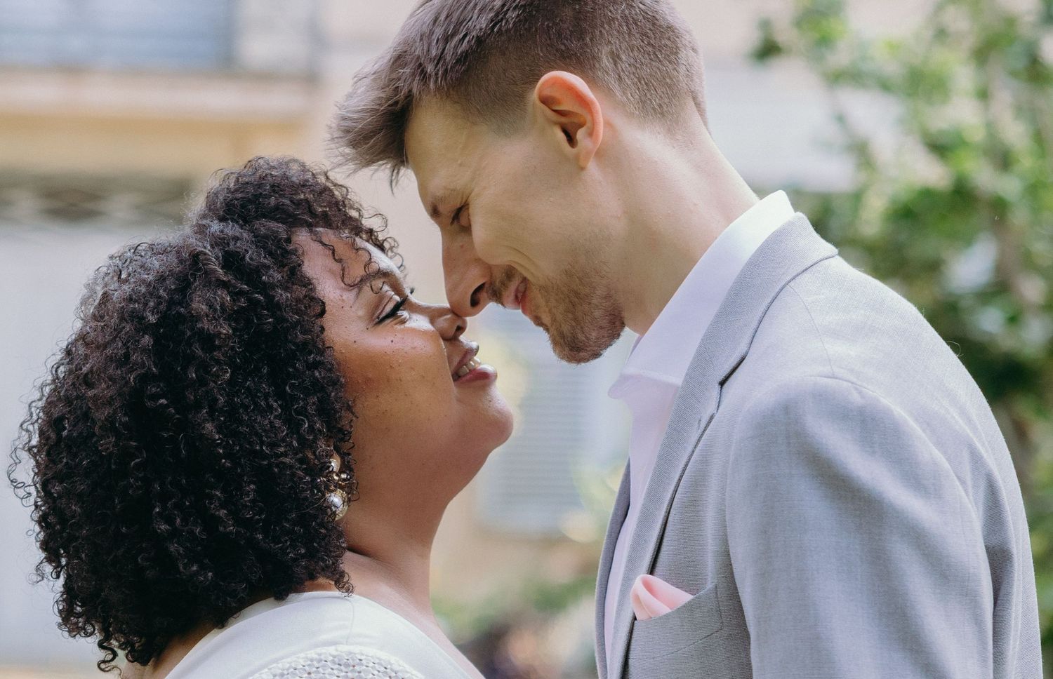 A couple in white and grey attire share an intimate moment outdoors.