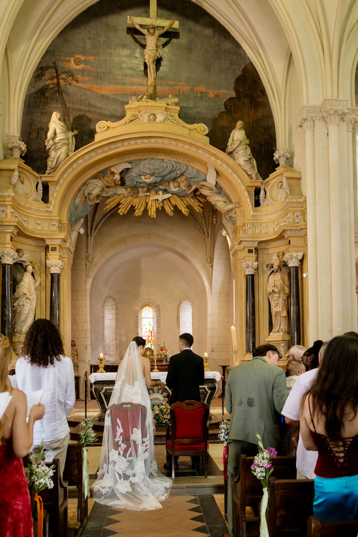 Bride and groom stand at ornate church altar during wedding ceremony with guests seated in pews.