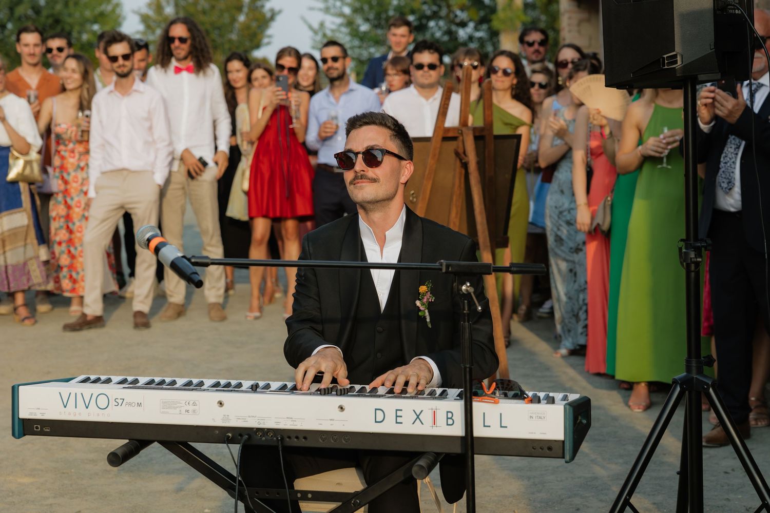 Musician playing a VIVO DEXIBELL keyboard at an outdoor wedding reception with guests watching.