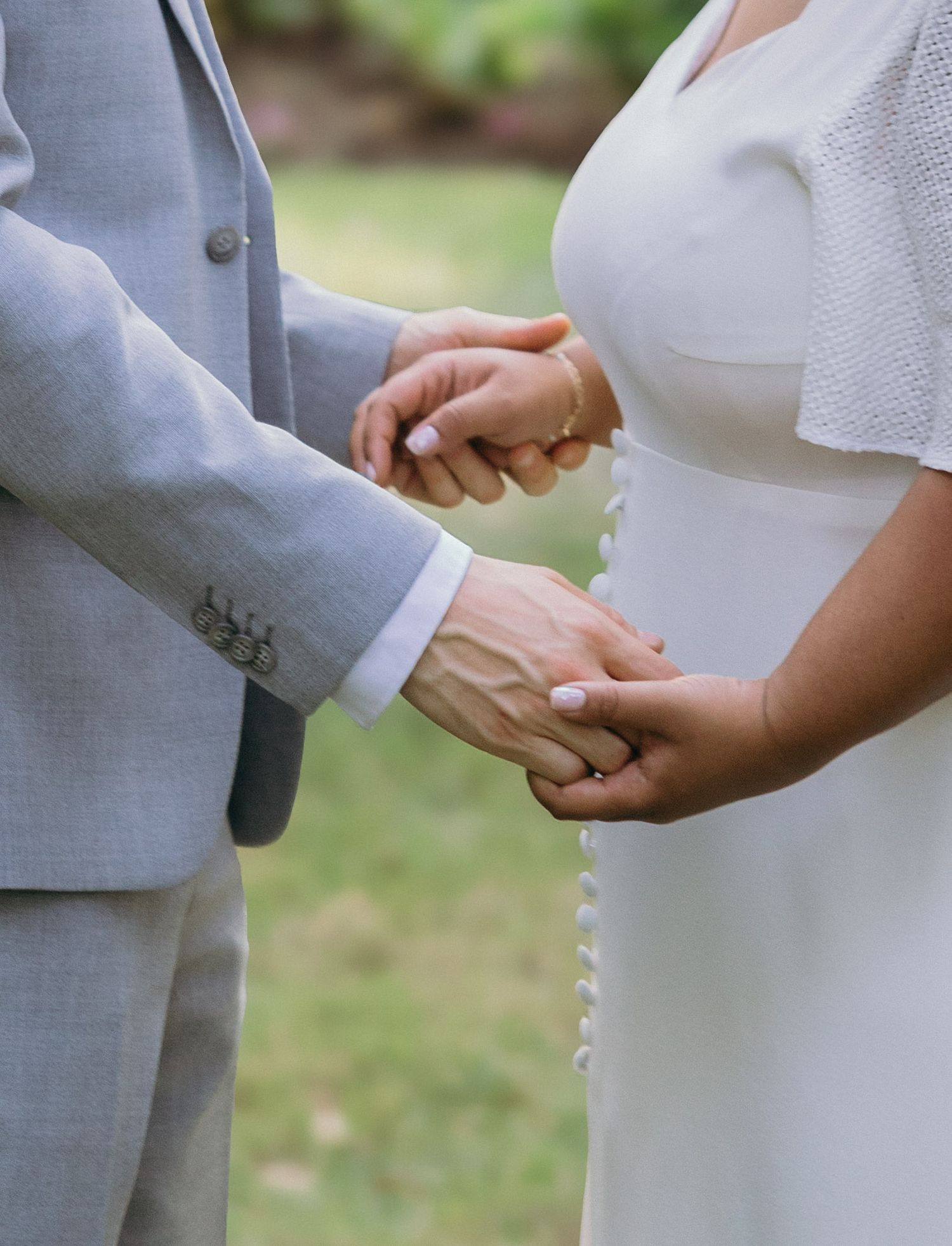 Close-up of hands tenderly clasping together in an outdoor garden setting.