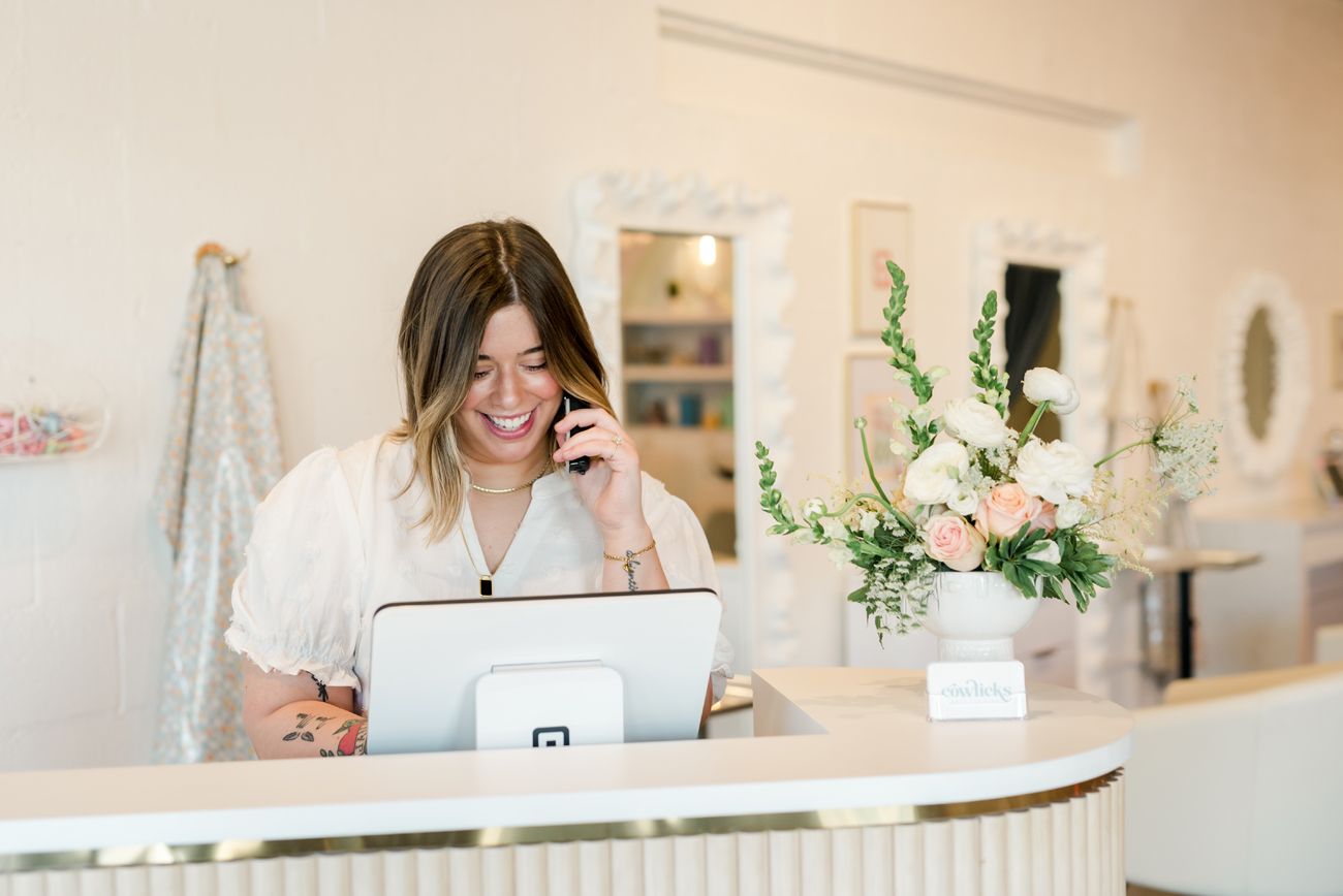 Person working at white desk with laptop and floral arrangement.