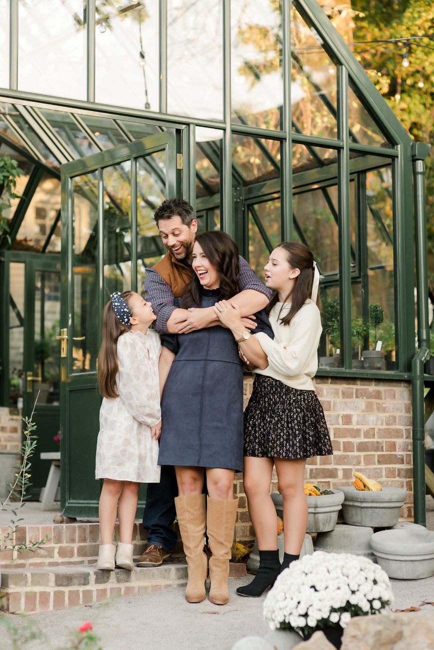 Family gathered around a greenhouse with brick foundation during a casual outdoor photoshoot.