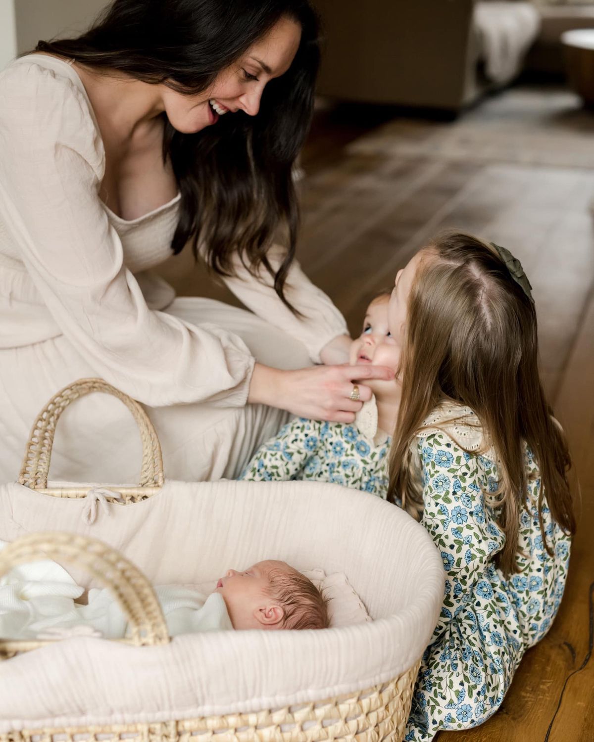 Sleeping newborn in white and pink outfit on ornate cream-colored chair.