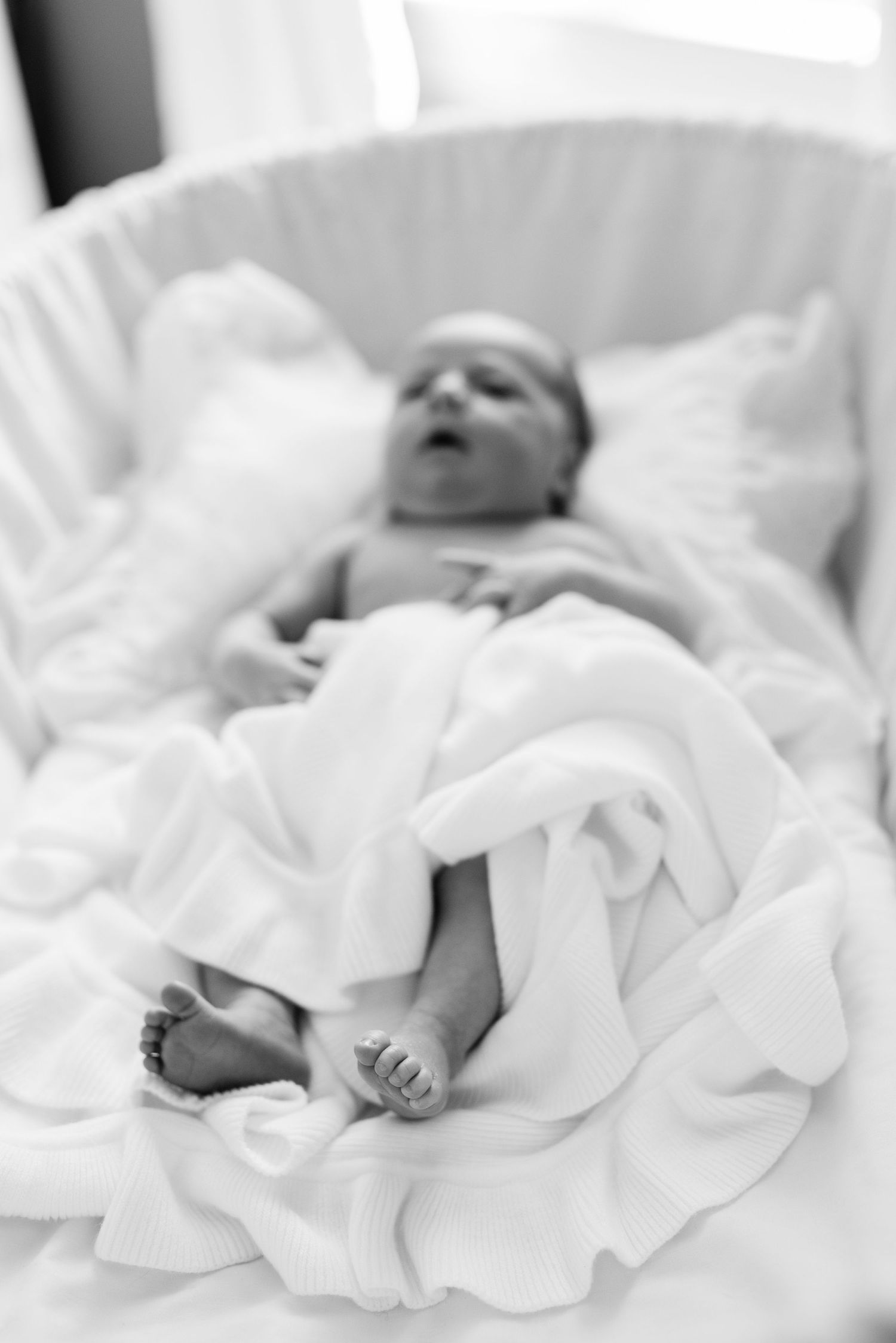 Black and white portrait of newborn baby sleeping on white blankets.