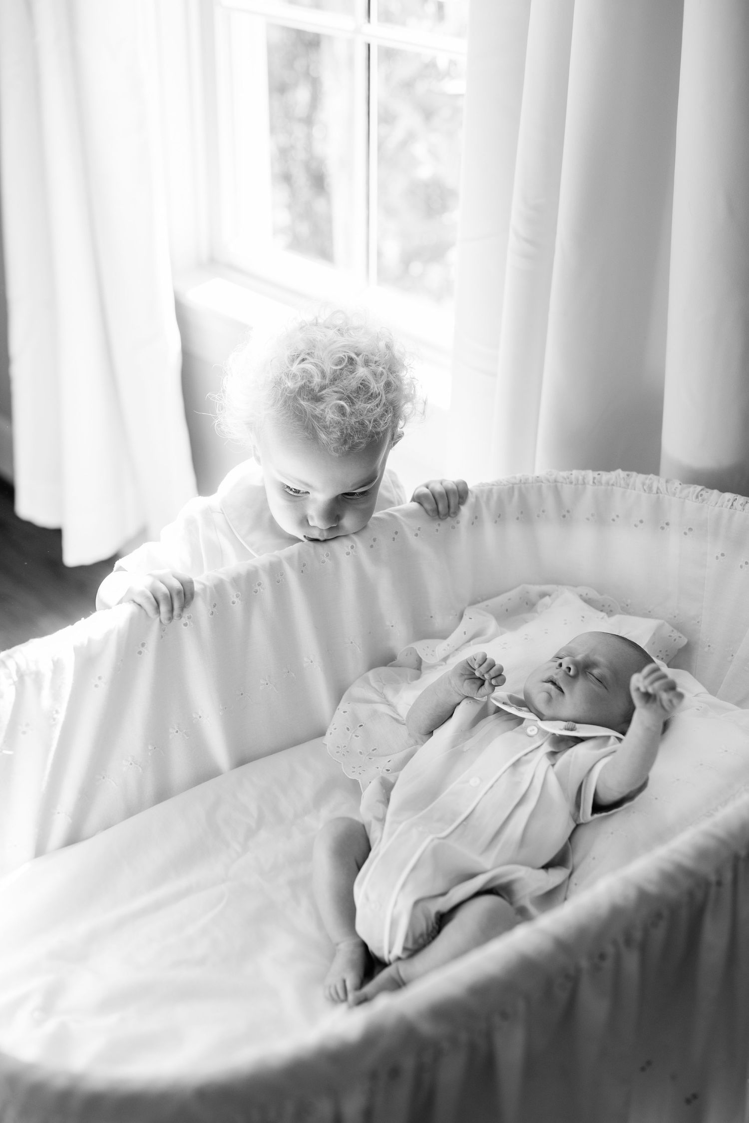 Black and white photo showing a child looking into a white bassinet.