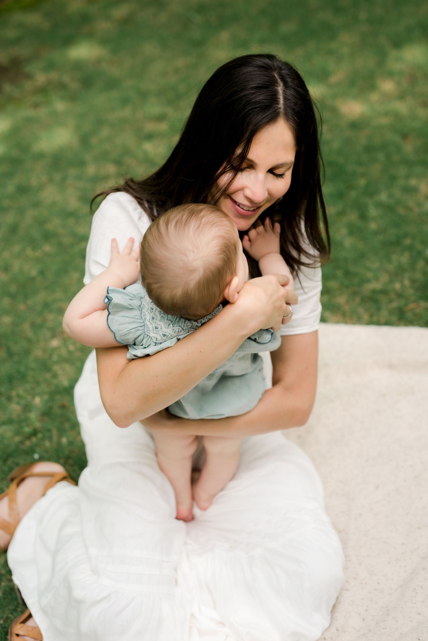 Tender moment between parent and baby on white blanket in outdoor garden setting.