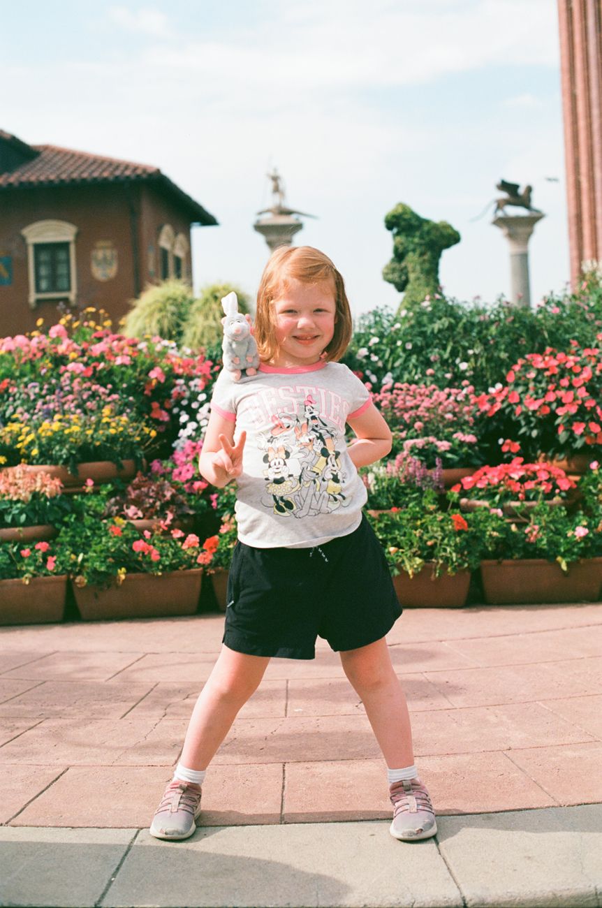 A cheerful child poses in front of pink flowers wearing a Disney character t-shirt and shorts.