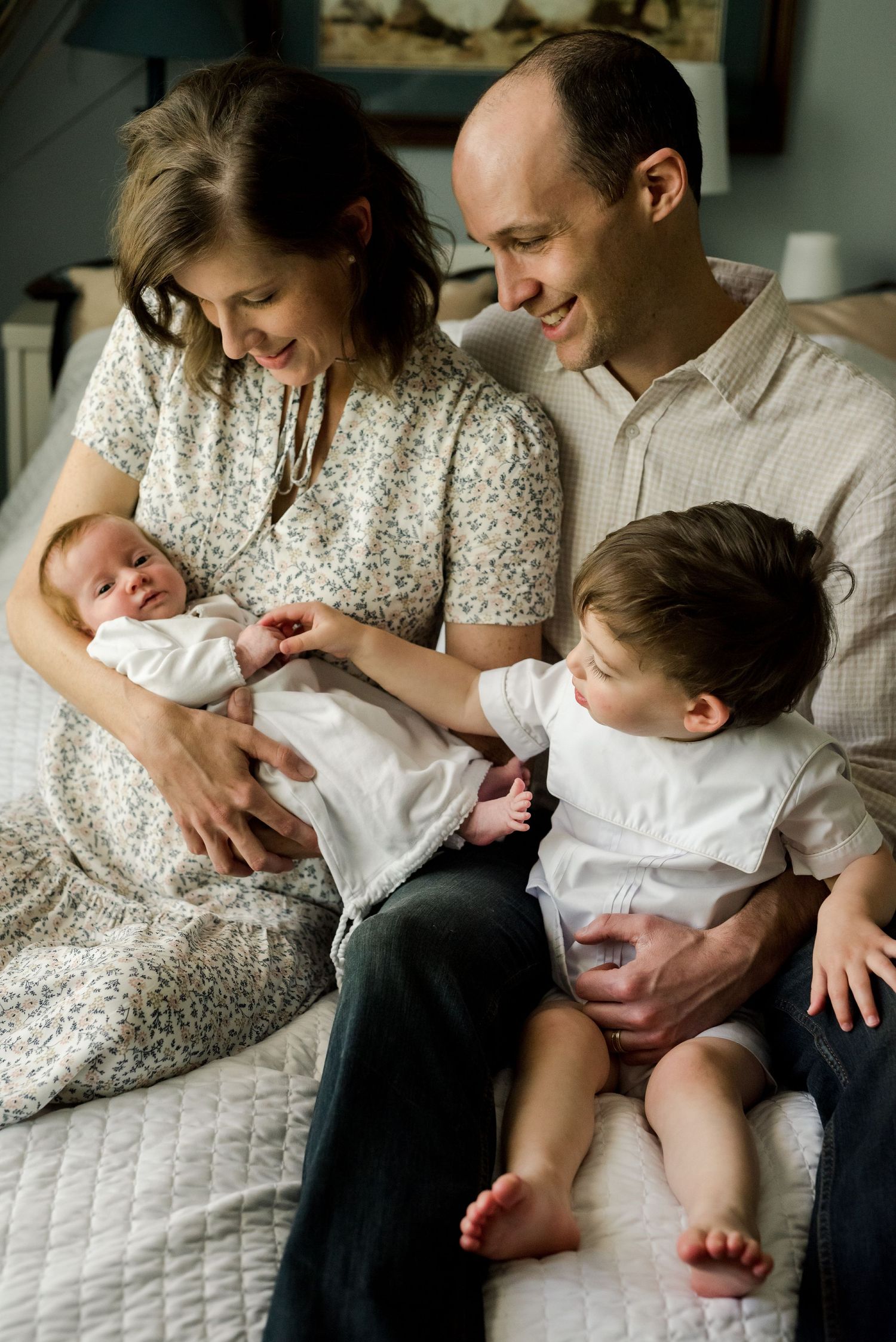A joyful indoor family moment with a newborn and toddler on white bedding.