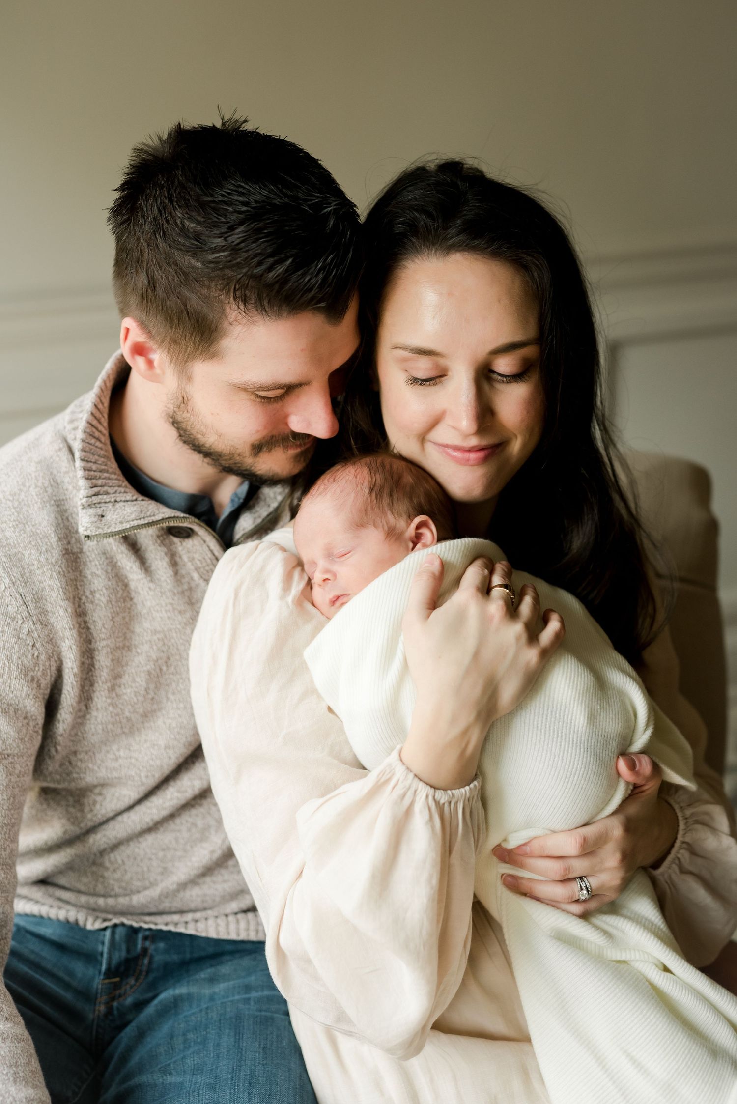 Intimate family moment with newborn baby being held and cuddled by parents in soft natural light.