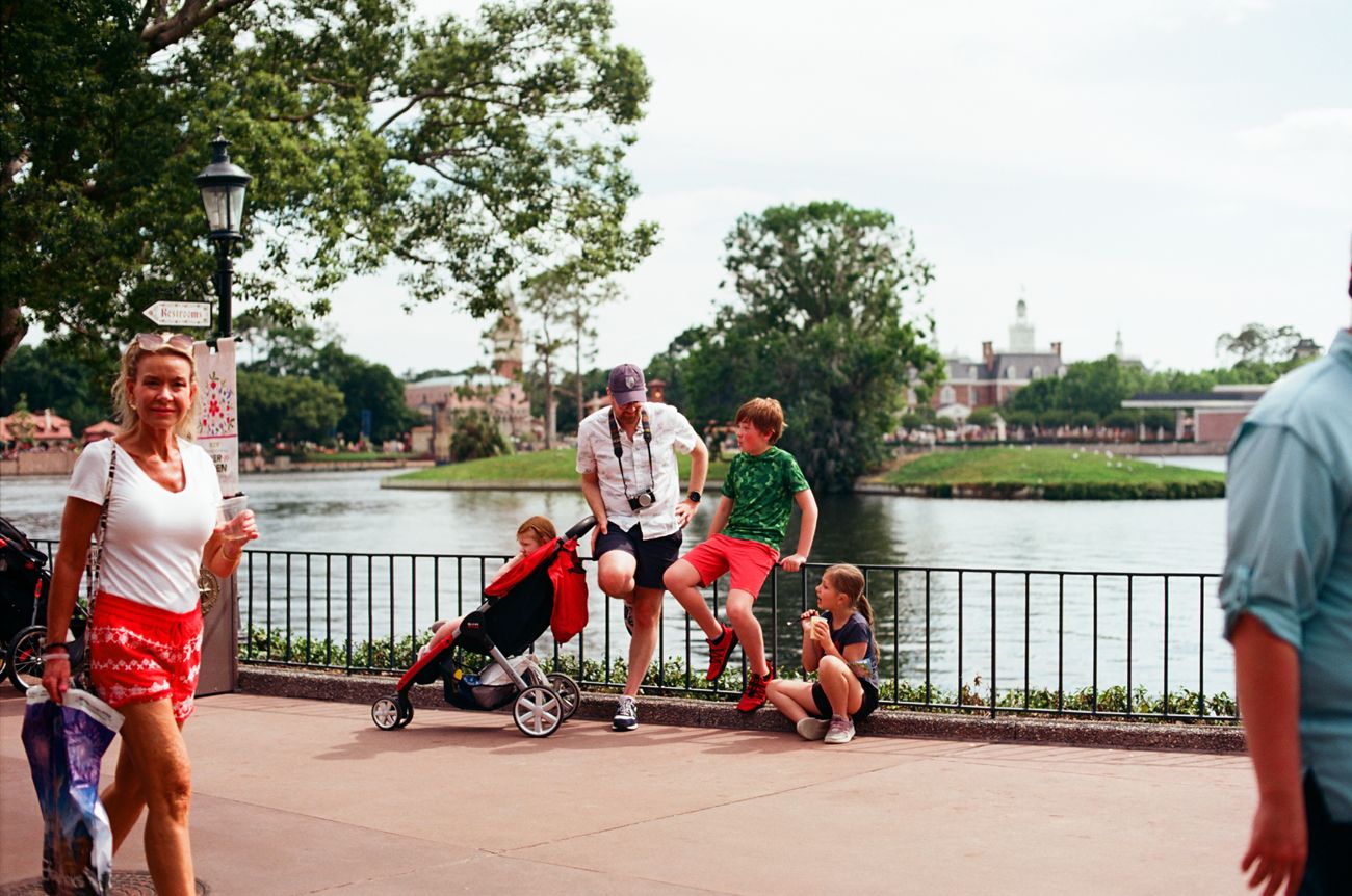 Visitors with strollers walking along a waterfront path at a theme park.