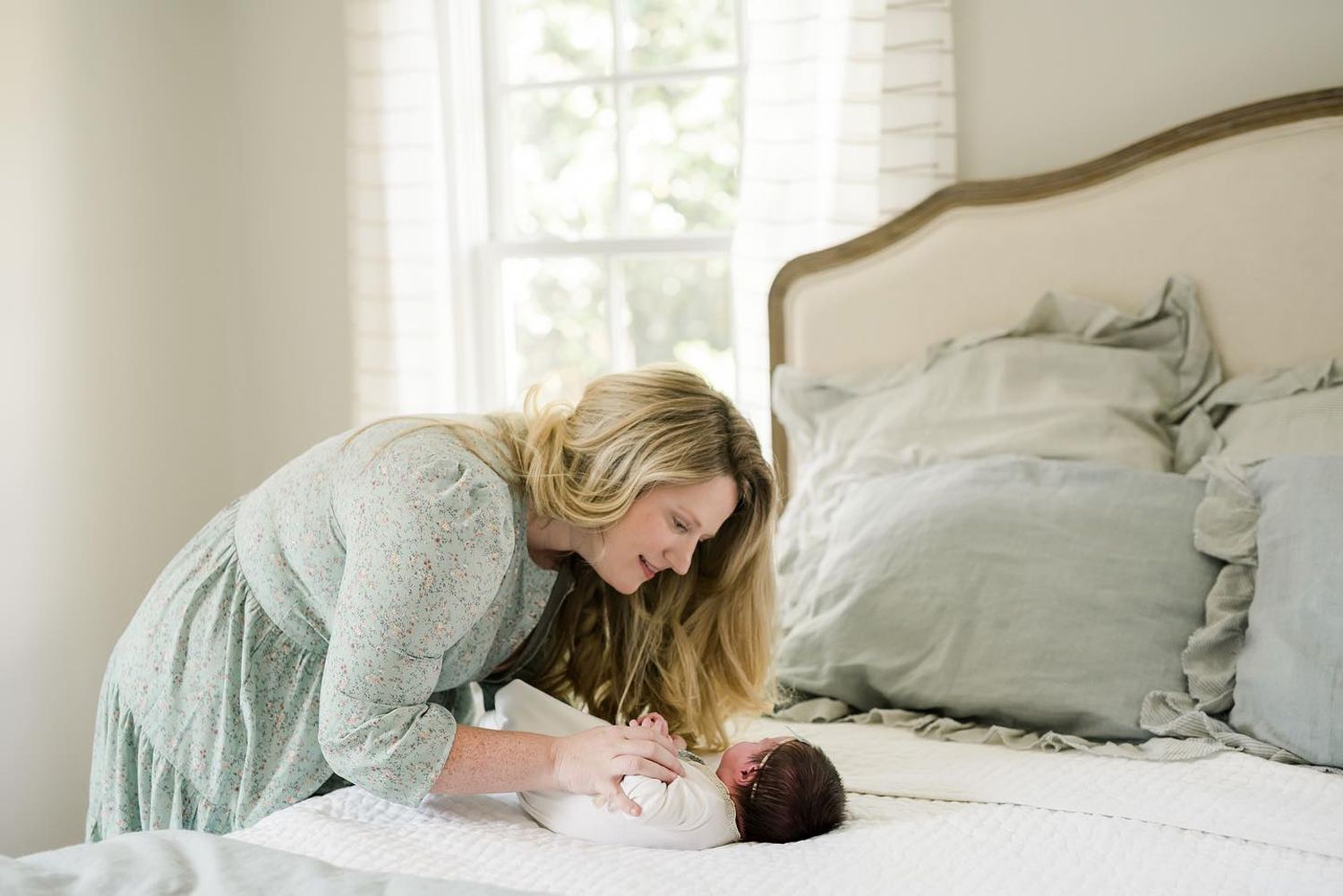 A tender moment between mother and newborn captured in soft natural light by a bedroom window.