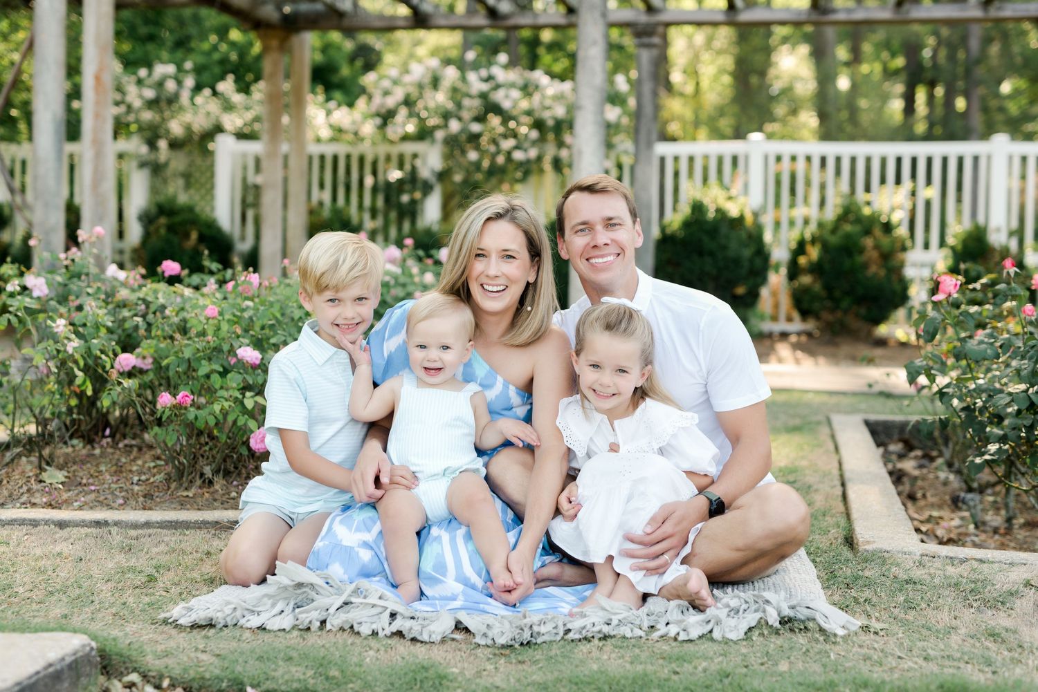 Family in coordinated blue and white outfits sitting on blanket in garden setting.