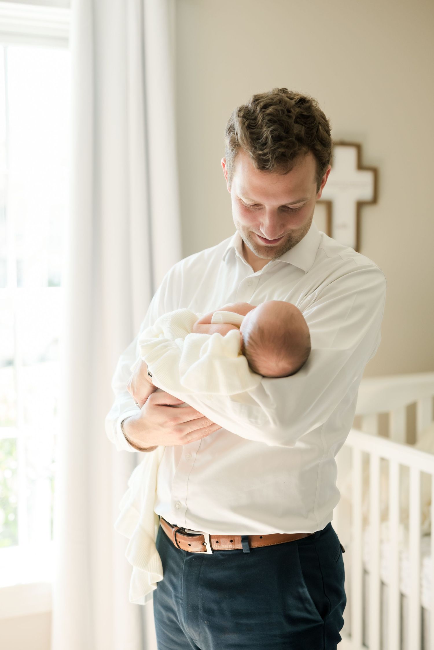 Father in white shirt tenderly holding newborn baby in nursery setting.