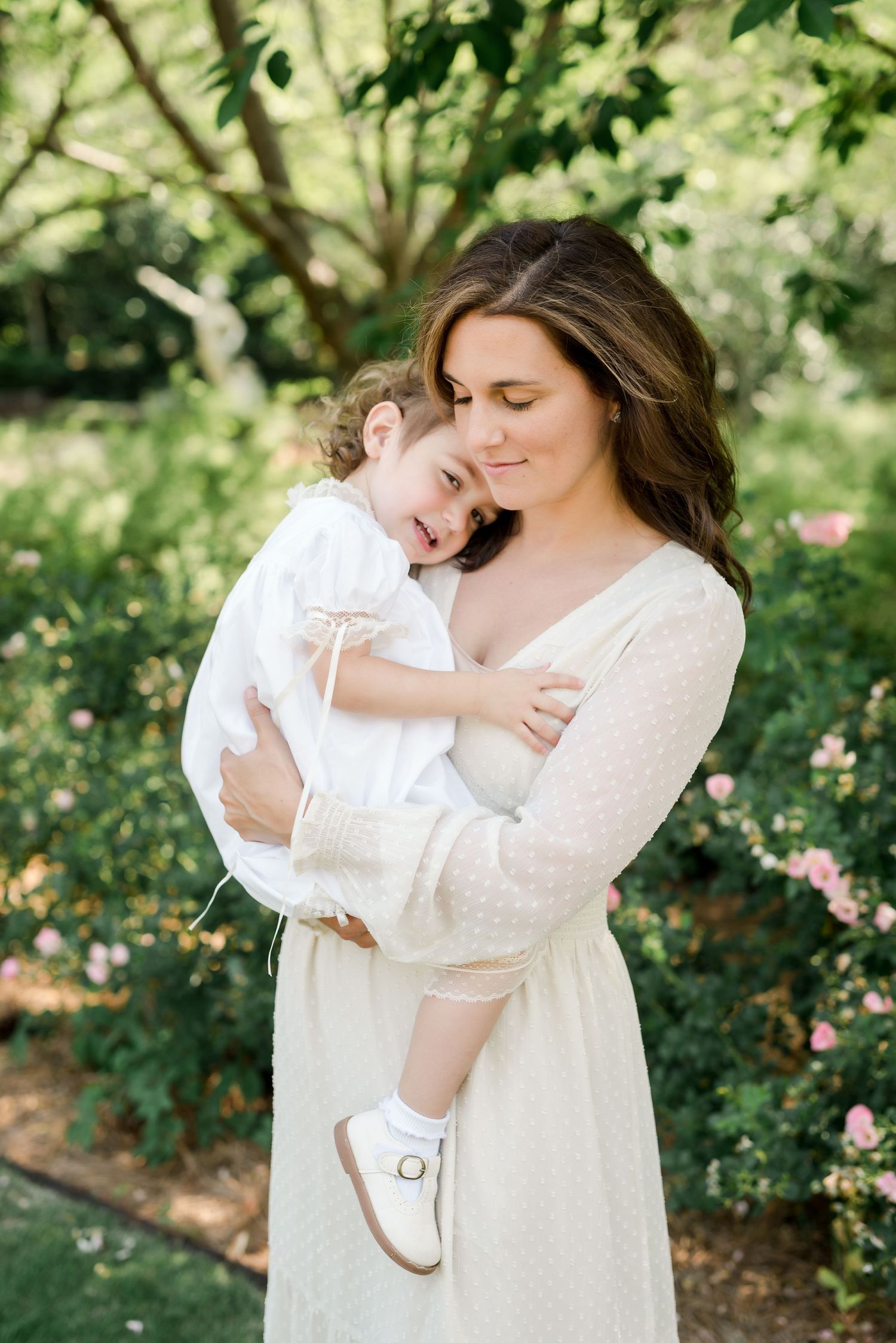 A tender embrace shared in a sunlit garden setting while wearing cream-colored clothing.