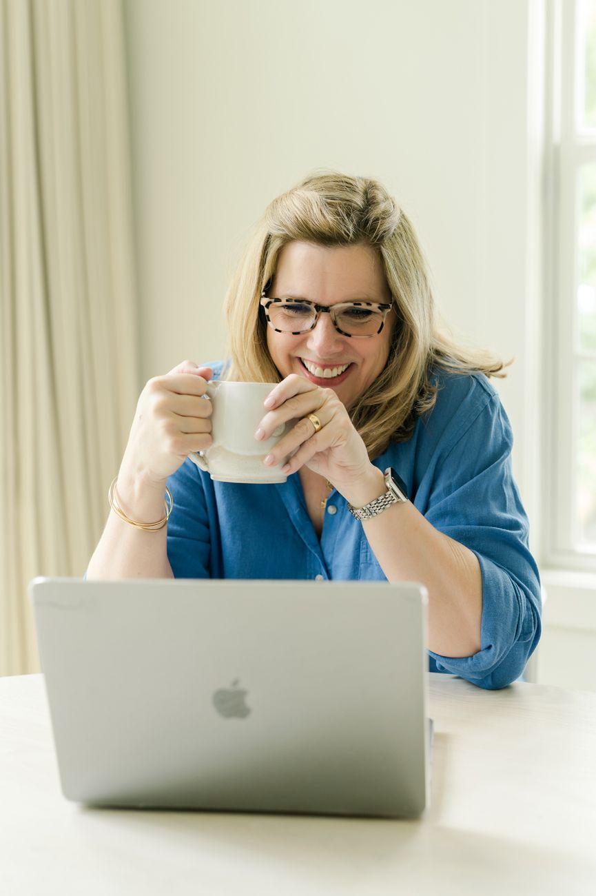 Person in blue shirt working and laughing while using MacBook laptop.
