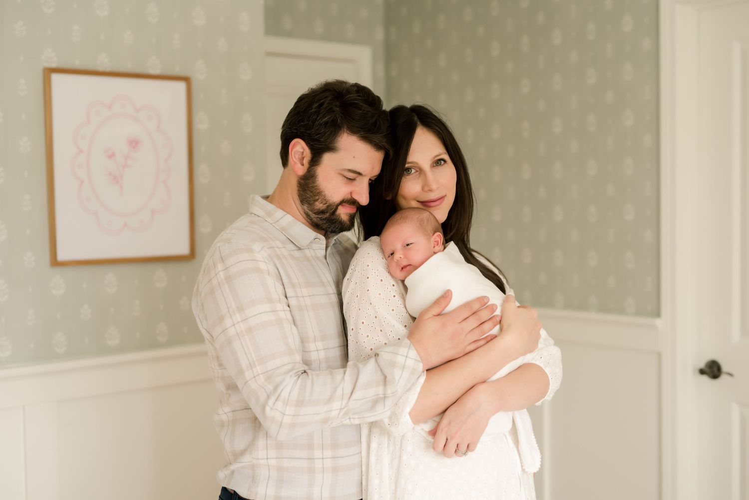 A couple shares a tender moment together in a light-filled nursery room with soft neutral decor.