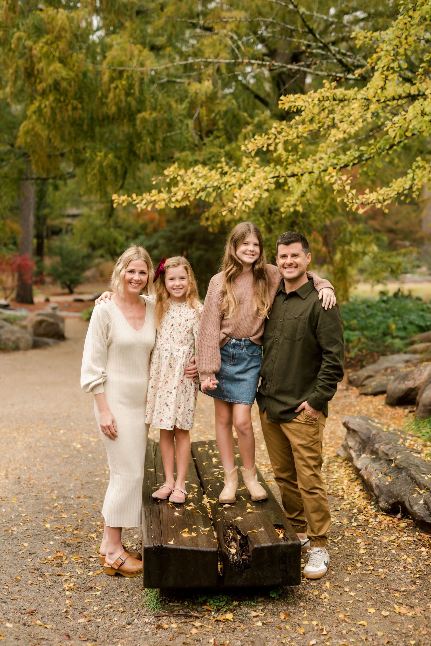 Family of four poses on wooden platform surrounded by autumn trees in a garden setting.