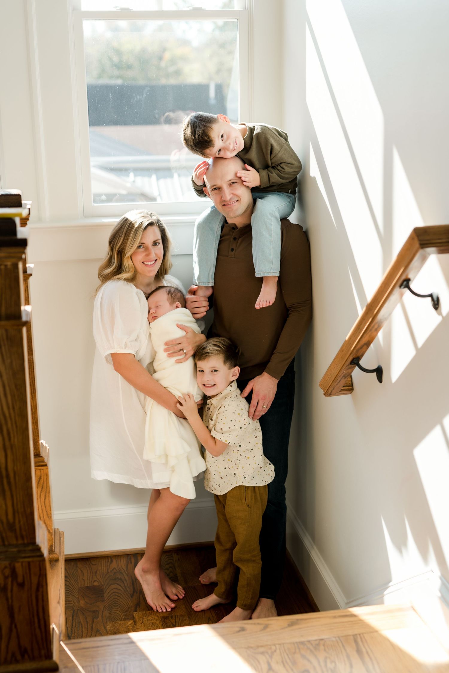 Loving family photo in stairwell with natural sunlight streaming through window.