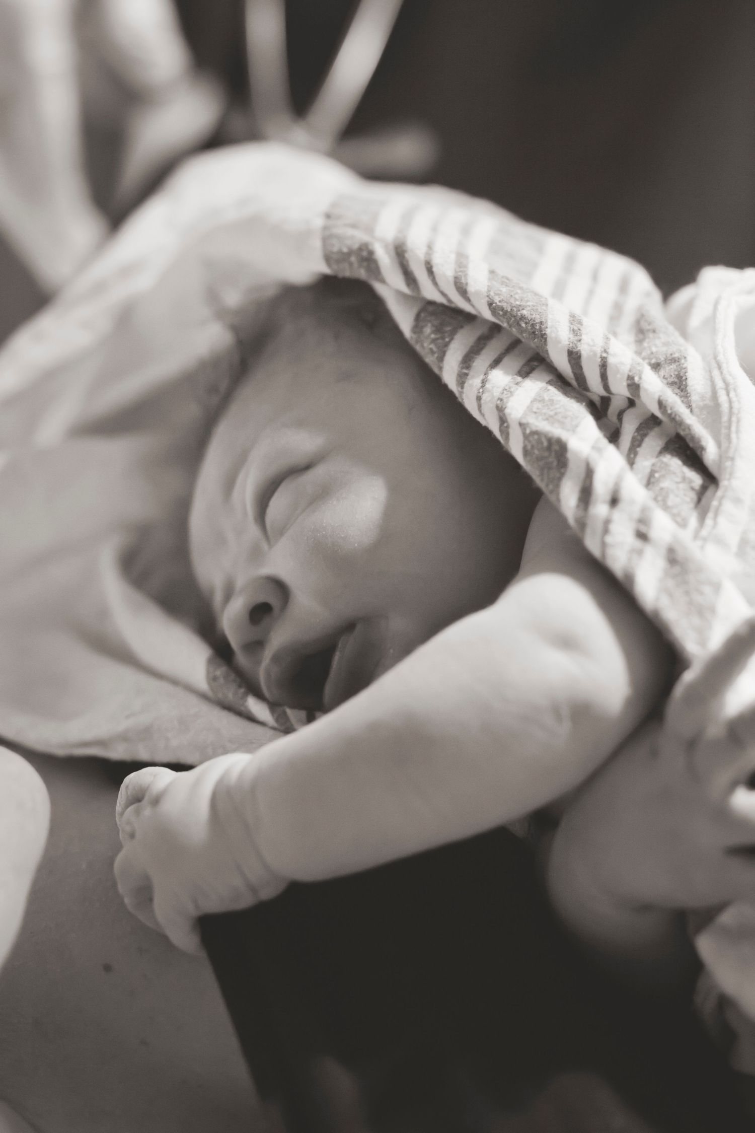 Peaceful newborn baby wrapped in blanket sleeping in black and white photo.