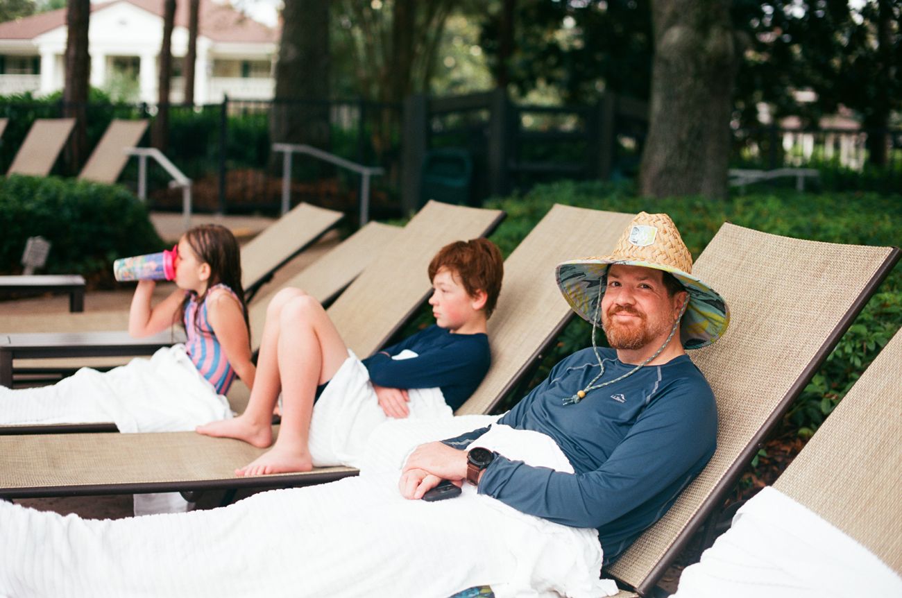 People relaxing on lounge chairs by a pool area surrounded by trees.