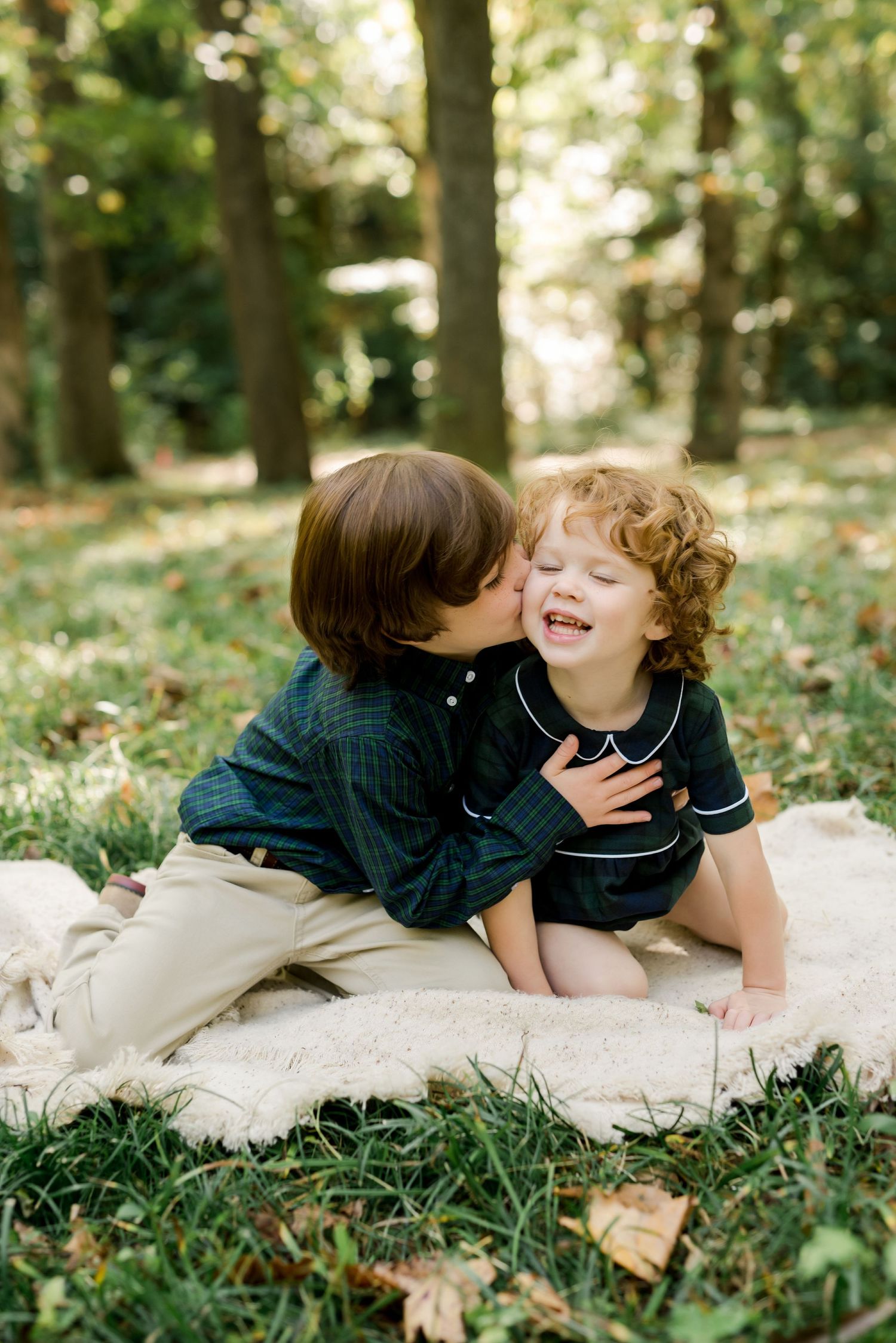 Two children sharing an affectionate moment while sitting on a blanket outdoors.