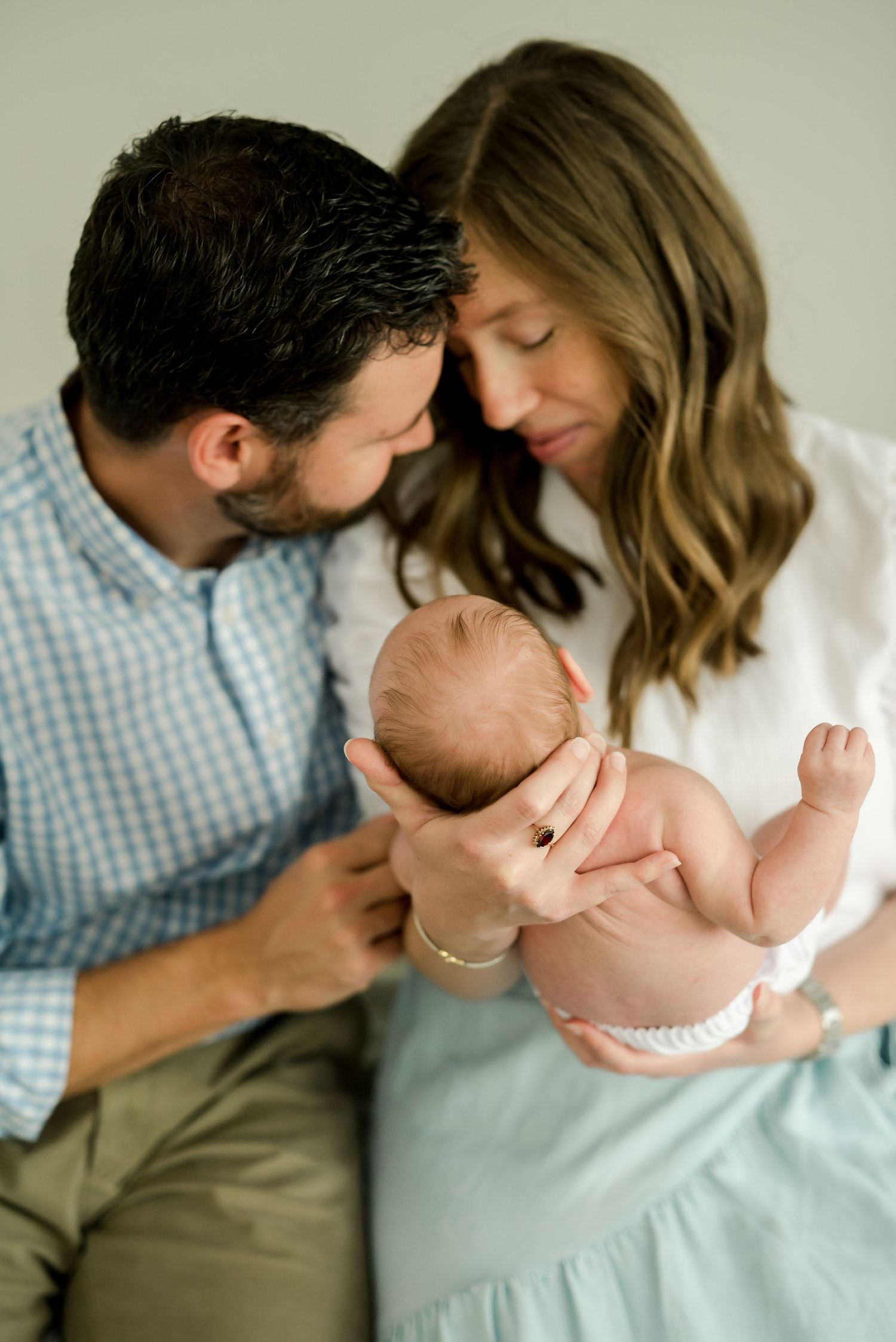 Intimate family portrait as parents gently hold their newborn baby on white bedding.