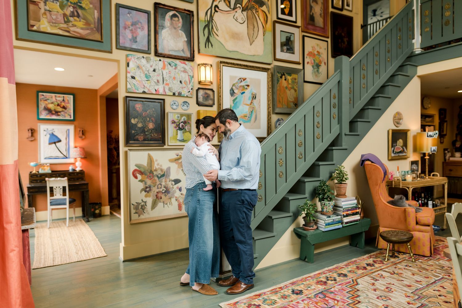 Couple in a cozy room filled with vintage artwork and a green staircase standing close together near a wall.