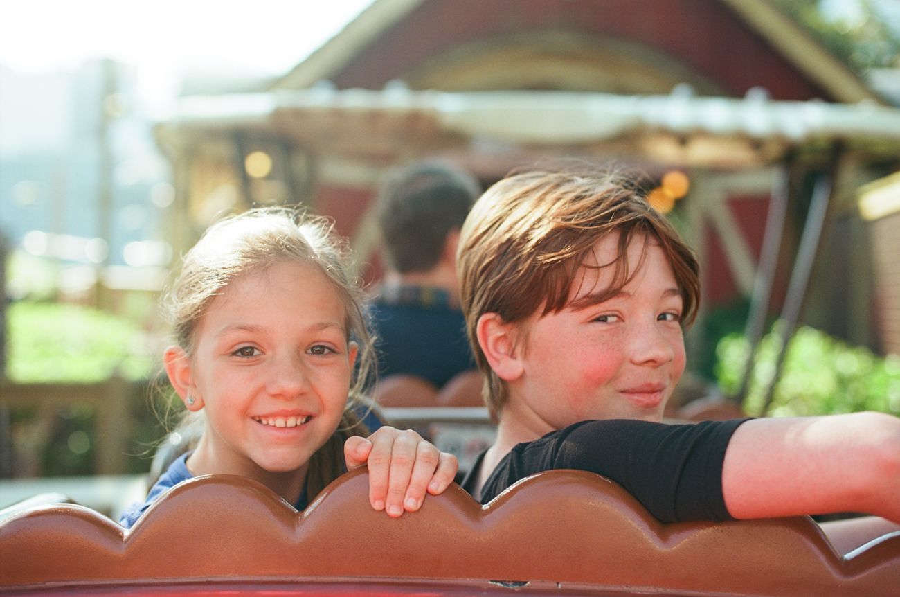 Two children sitting together and smiling on an amusement park ride.