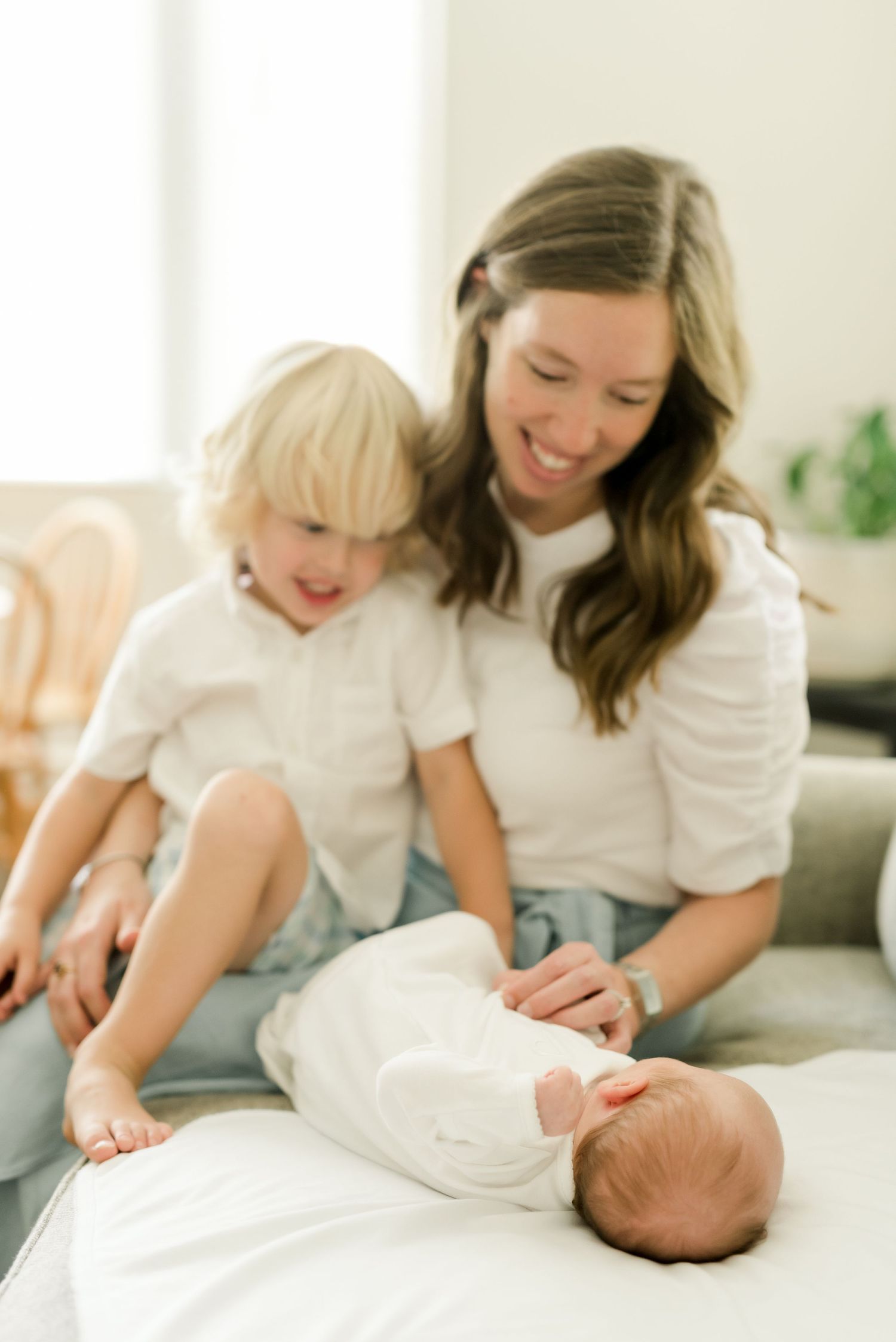 A tender family moment on the couch as they interact with their newborn baby in white clothing.