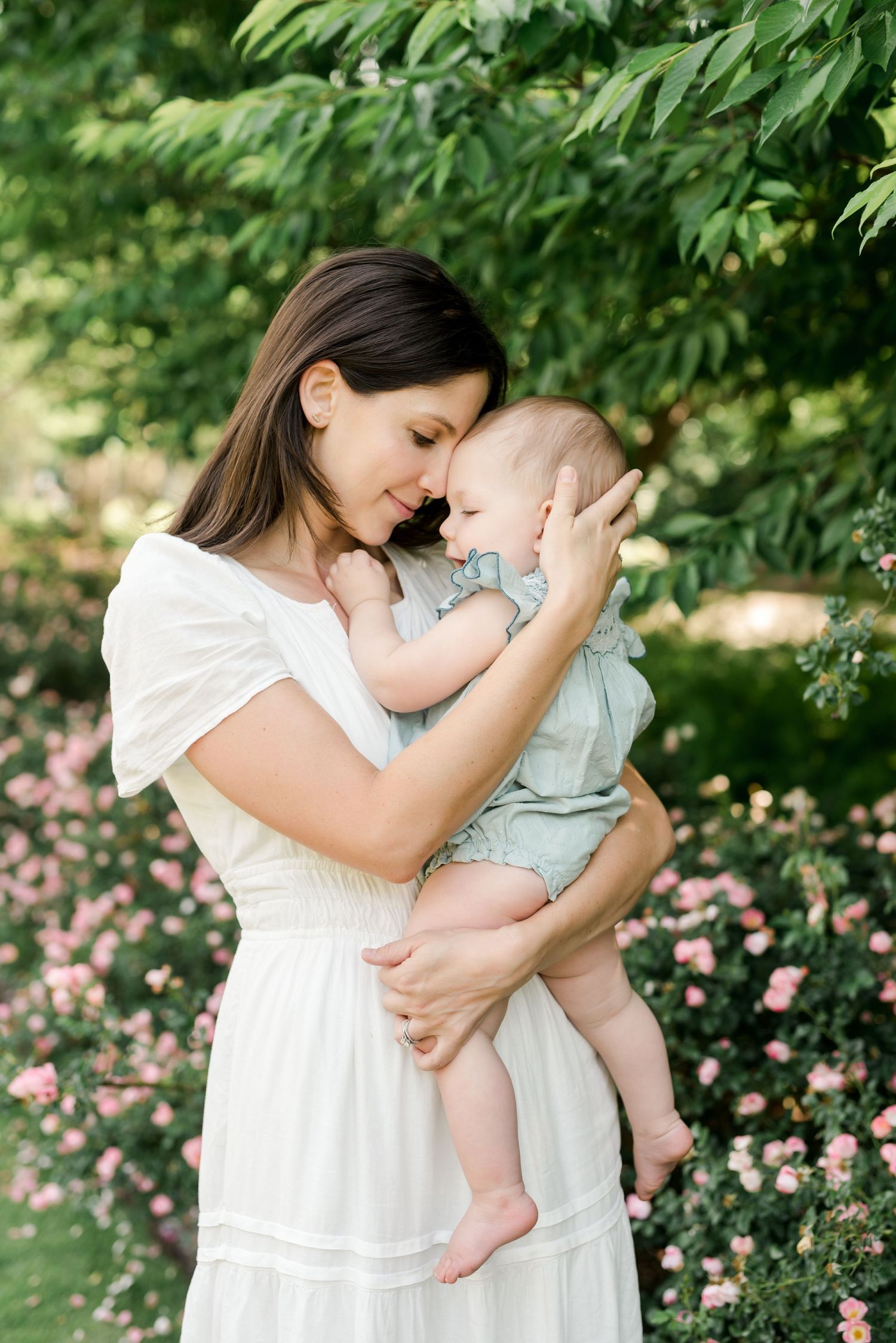 Intimate moment between mother and baby by flowering garden with soft natural lighting.