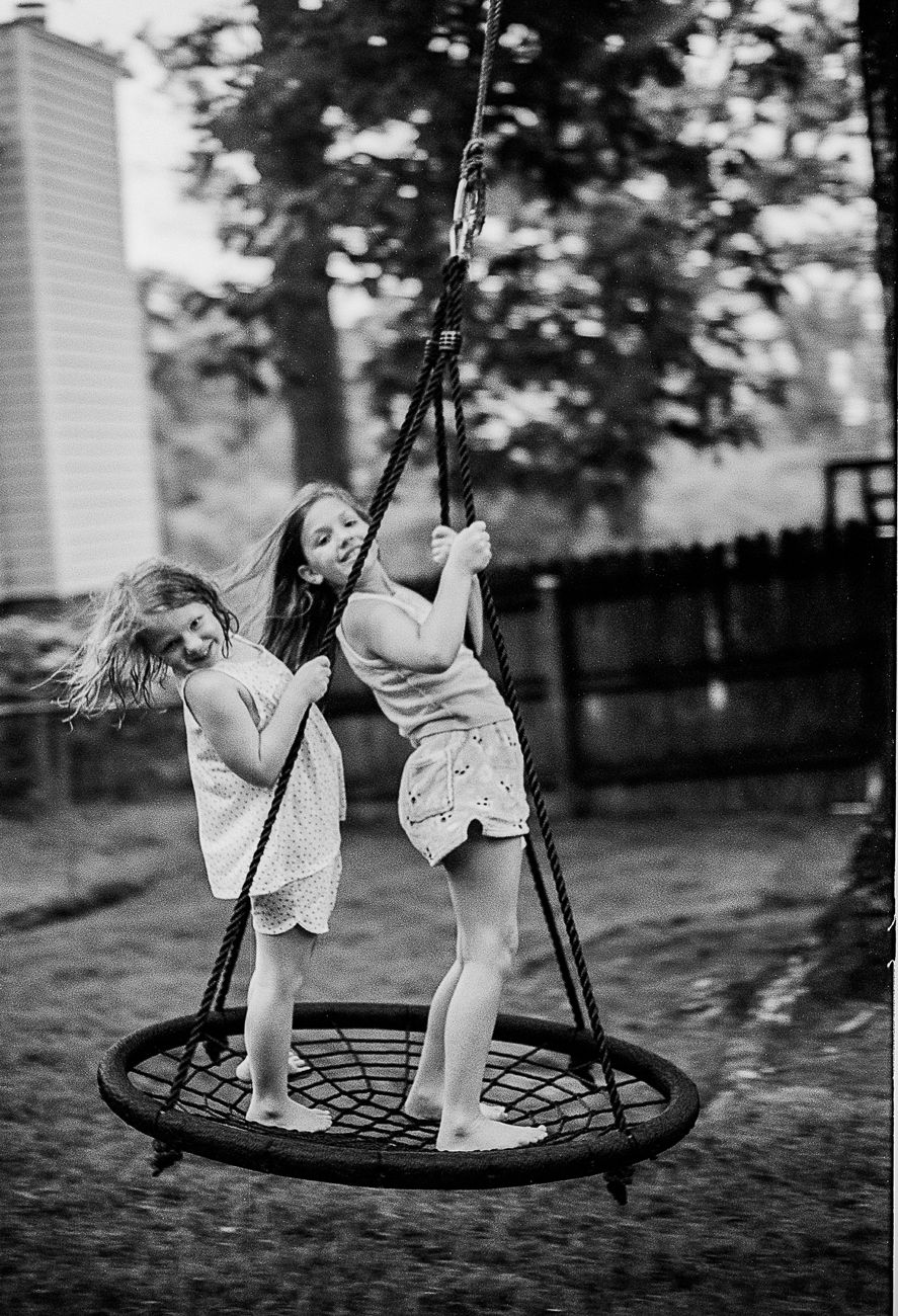 Black and white photo of children playing on a spider web swing in a backyard.